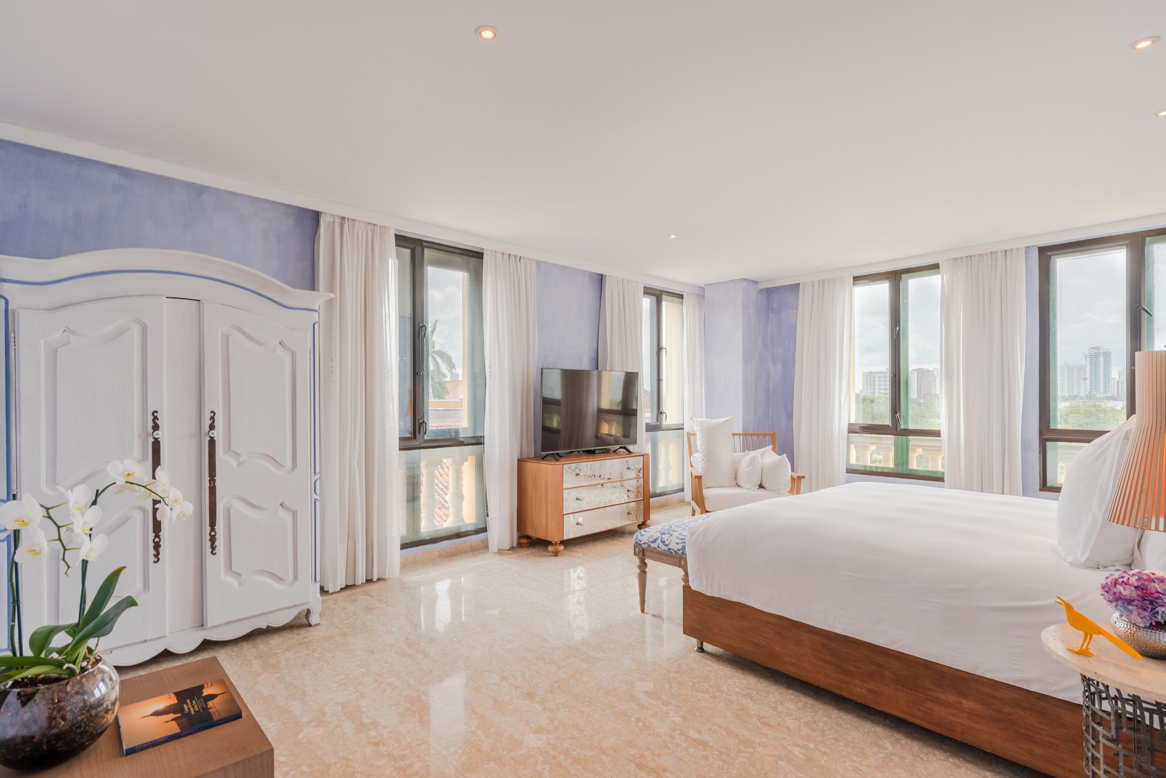 A hotel room with a large bed, a television, a dresser, and a view of the city.