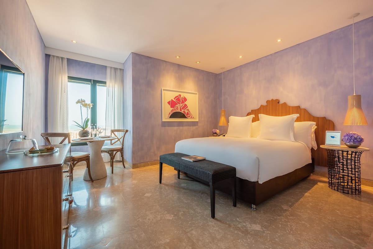 Een moderne hotelkamer met een groot bed, een zithoek met een tafel en stoelen, en uitzicht op het landschap door het raam.