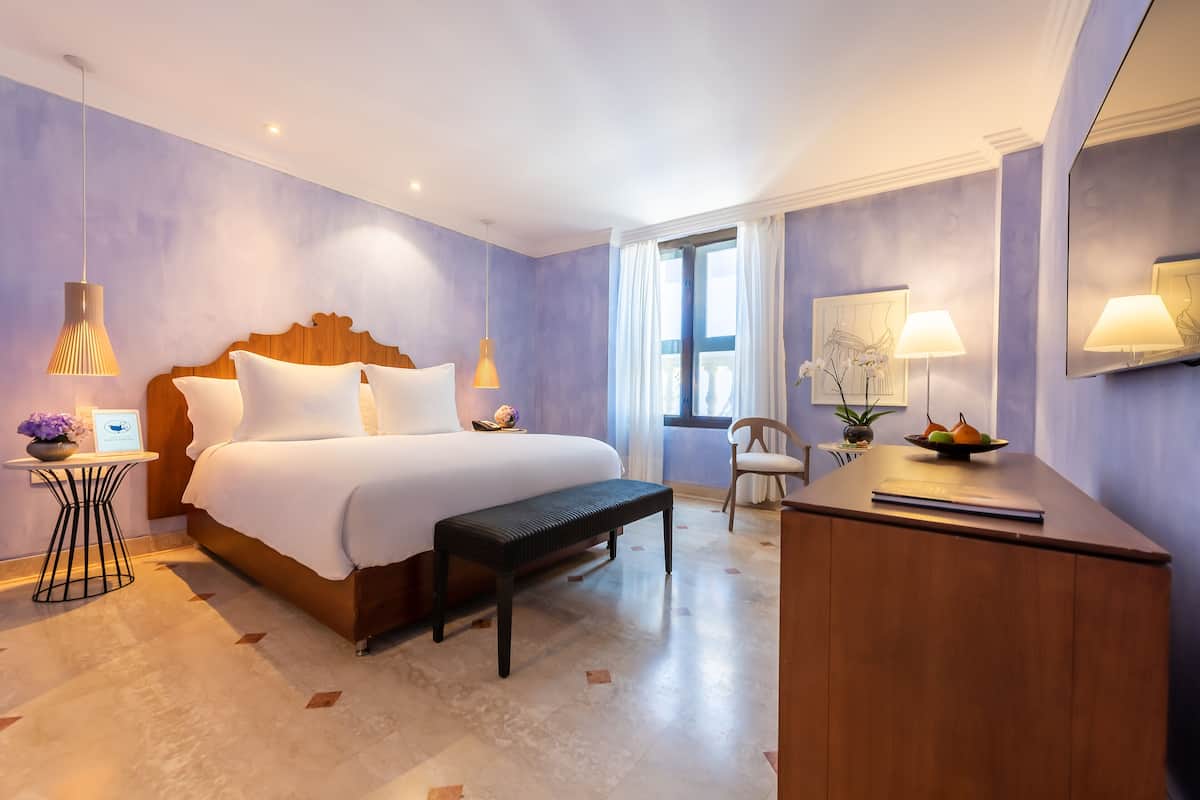 Een moderne hotelkamer met een groot bed, nachtkastjes, een bankje, een bureau en een stoel.