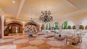 Un hall d’entrée spacieux avec un sol en marbre, des canapés blancs, un grand arrangement floral au centre et un lustre imposant.