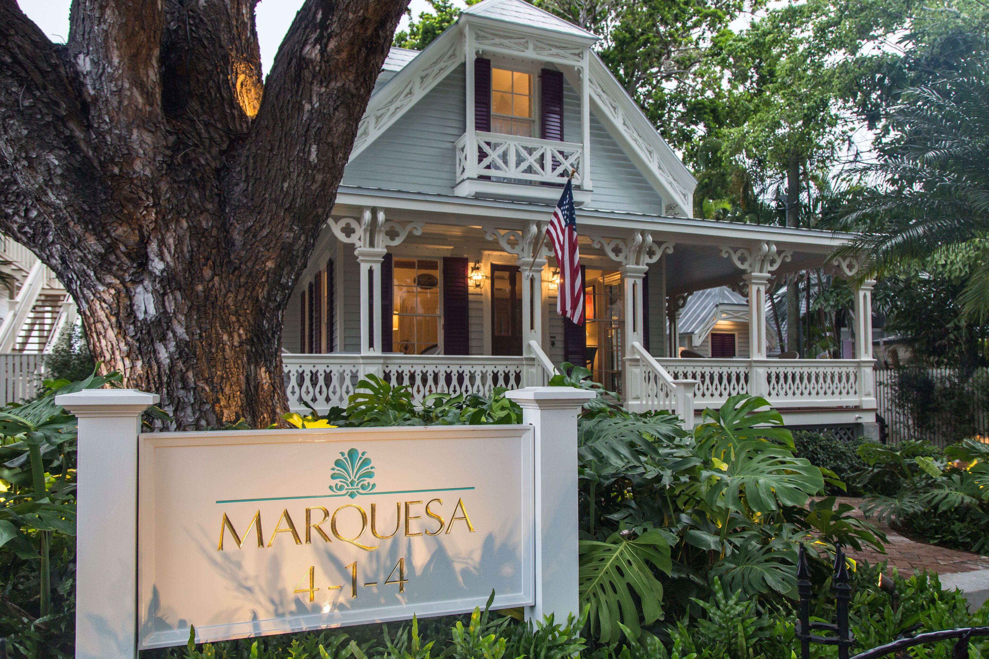 A historic house with a porch, an American flag, and a sign that reads "MARQUESAS 4-14".