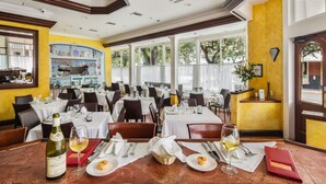 A restaurant with multiple tables set for dining, a wine bottle, and a glass of wine on the table.