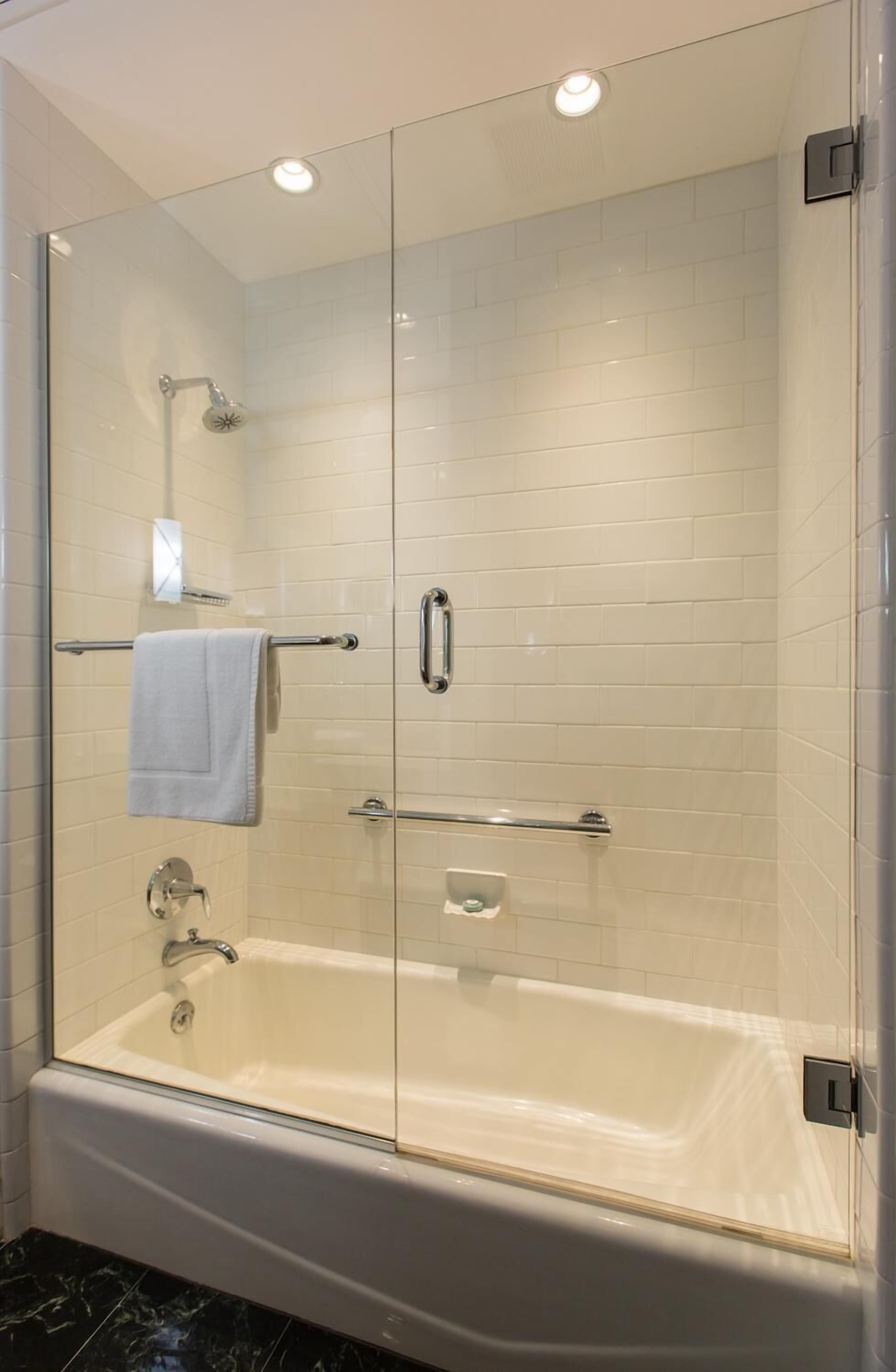 A walk-in glass shower with a white tiled wall, a glass door, and a handheld showerhead.