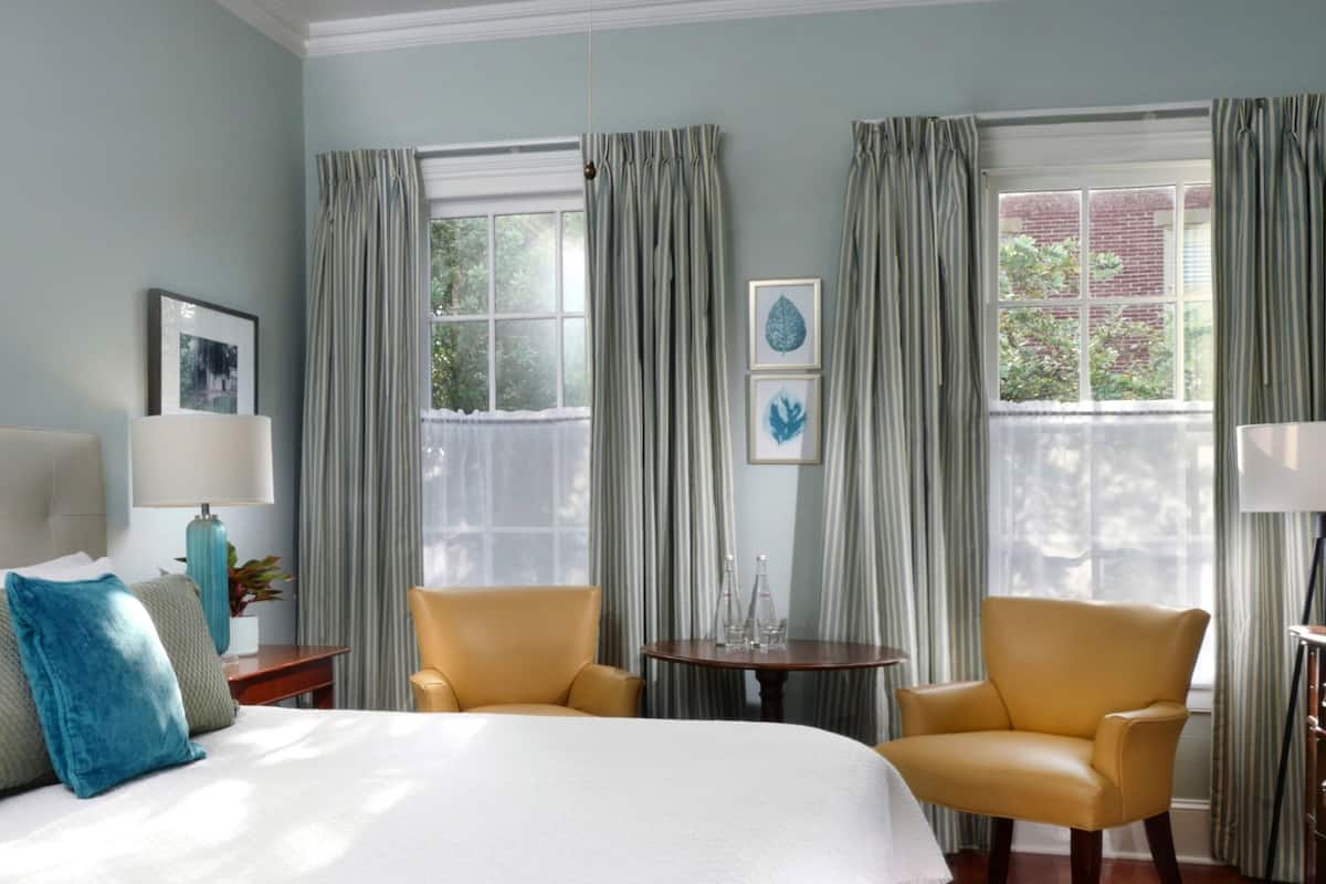 A hotel room with a bed, two chairs, a small table, and a window with curtains.