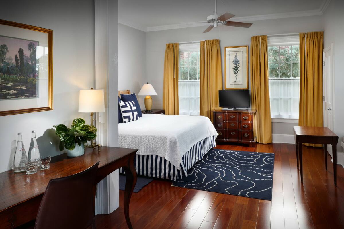 A hotel room with a bed, a desk, a television, a dresser, and a window with curtains.
