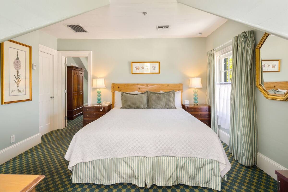 A bedroom with a large bed, two bedside tables with lamps, a dresser, and a mirror on the wall.