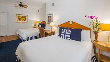 A hotel room with a large bed, two smaller beds, a desk, and a ceiling fan.