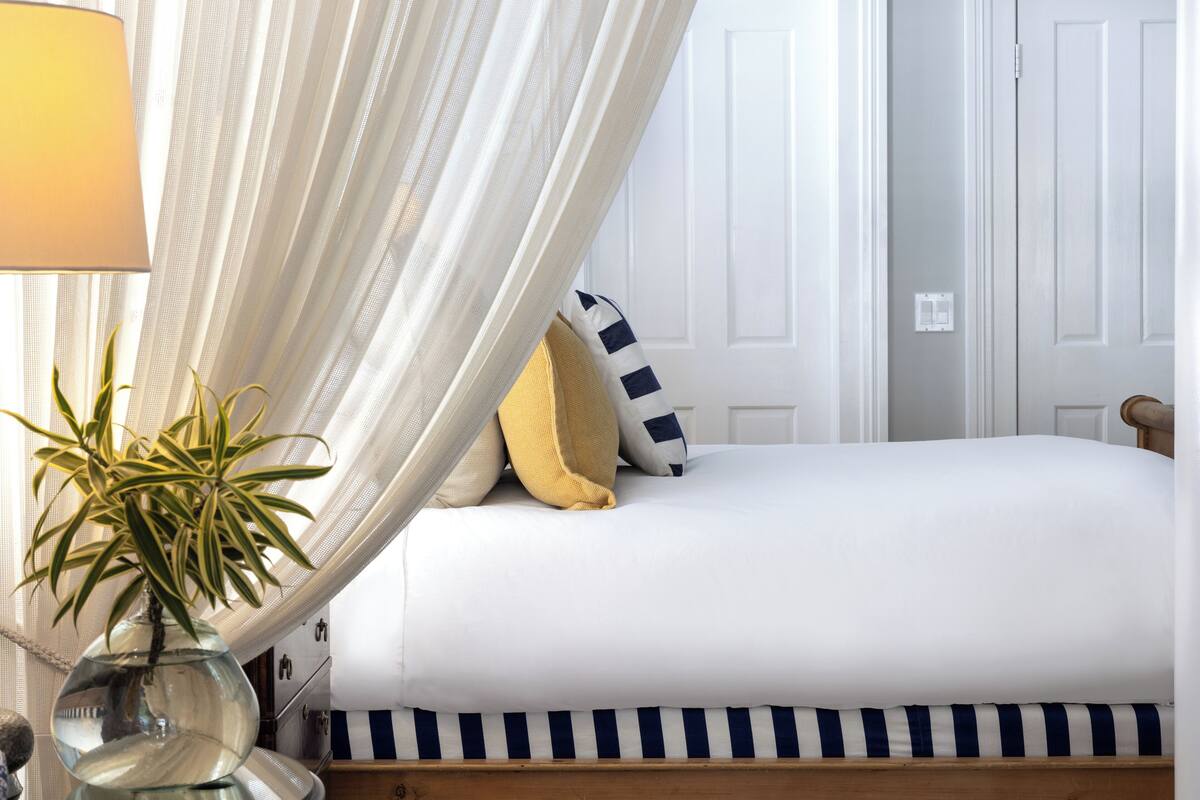A bedroom with a bed, a bedside lamp, a potted plant, and a door.