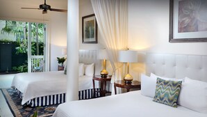 A hotel room with two beds, a ceiling fan, a large window with a view of palm trees, and a painting on the wall.