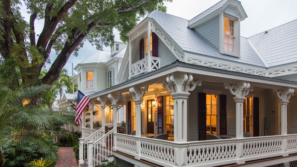 A two-story house with a covered porch, a brick pathway, and a large tree.