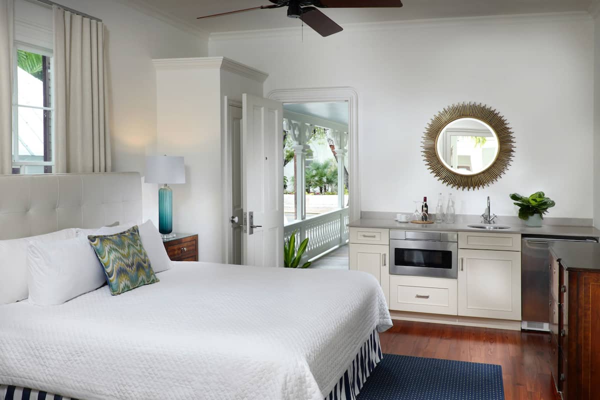 A bedroom with a bed, a nightstand, a lamp, a dresser, a mirror, and a view of the outdoors.