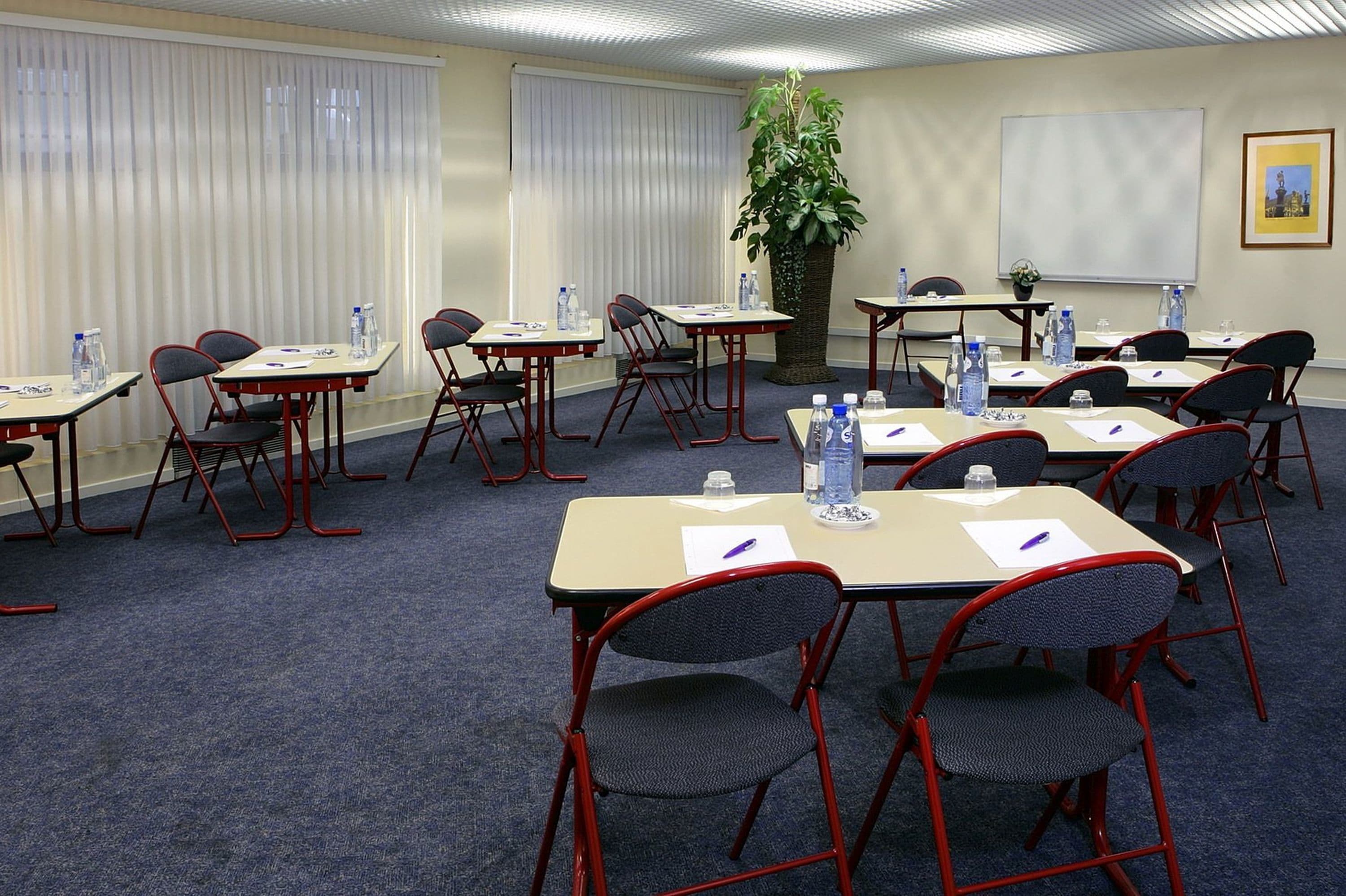 A conference room with tables and chairs, water bottles, and a projector screen.