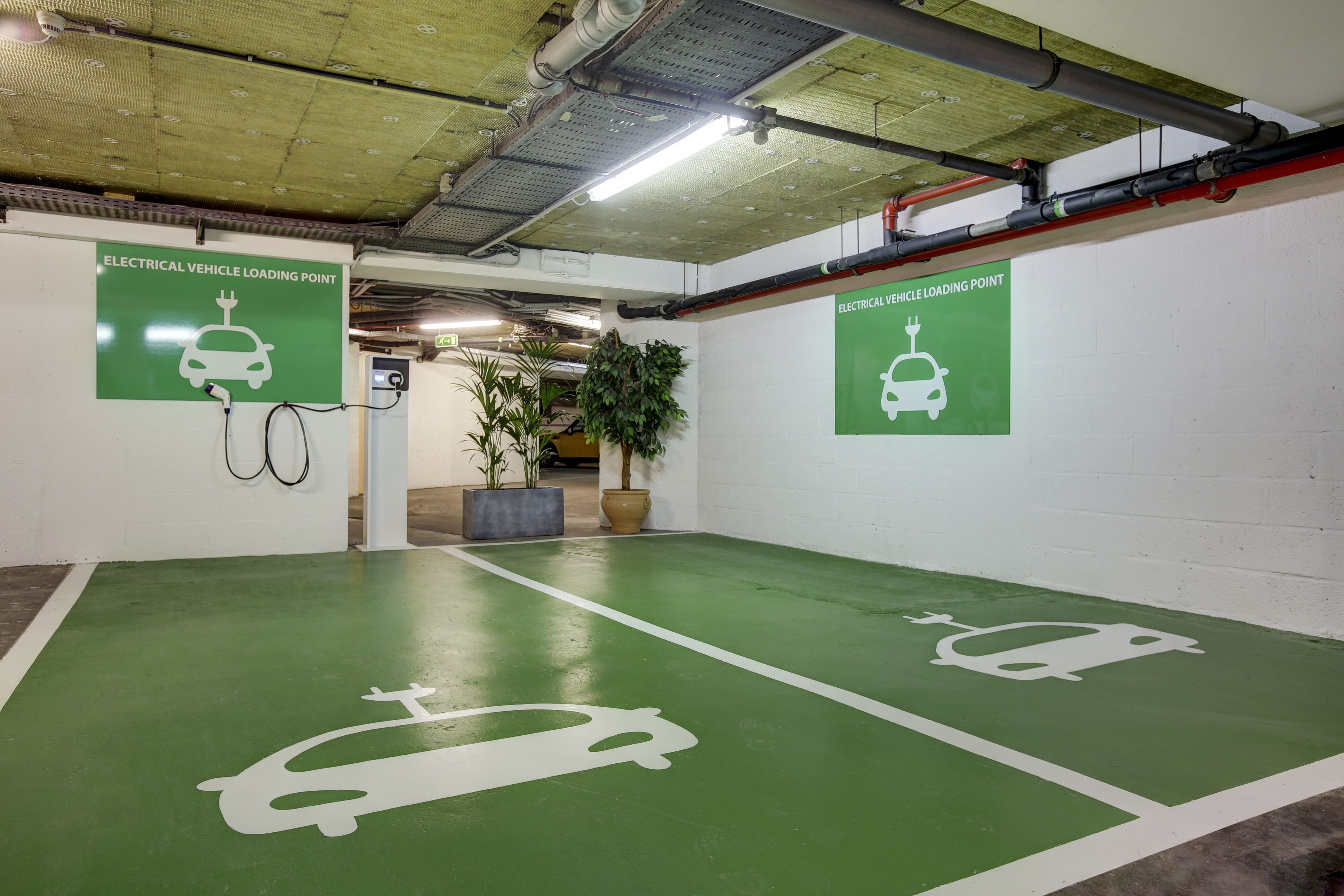 An indoor parking area with green flooring, white parking lines, and signs indicating electrical vehicle loading points.