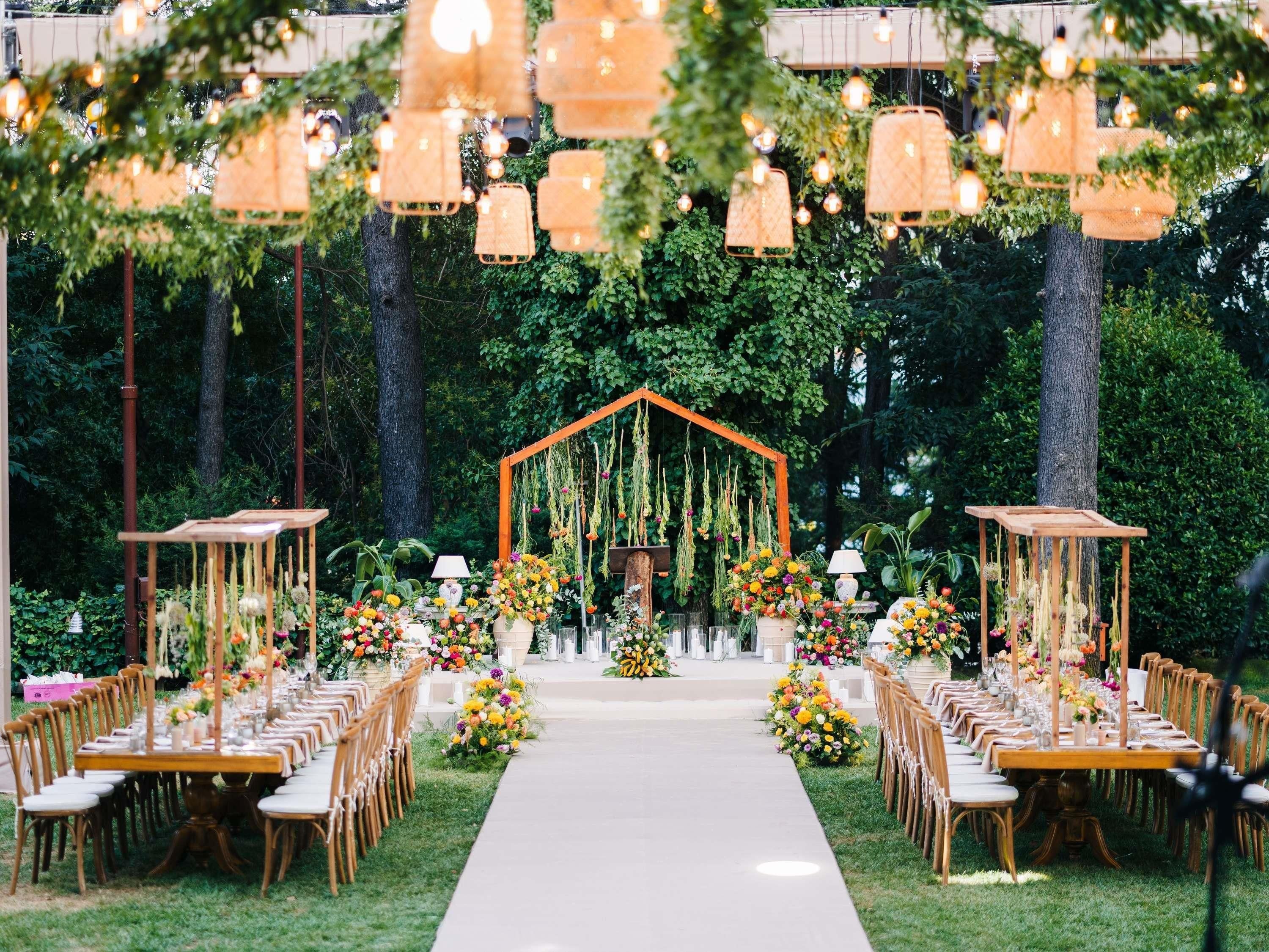 An outdoor wedding venue with a central aisle, floral arrangements, and hanging light fixtures.