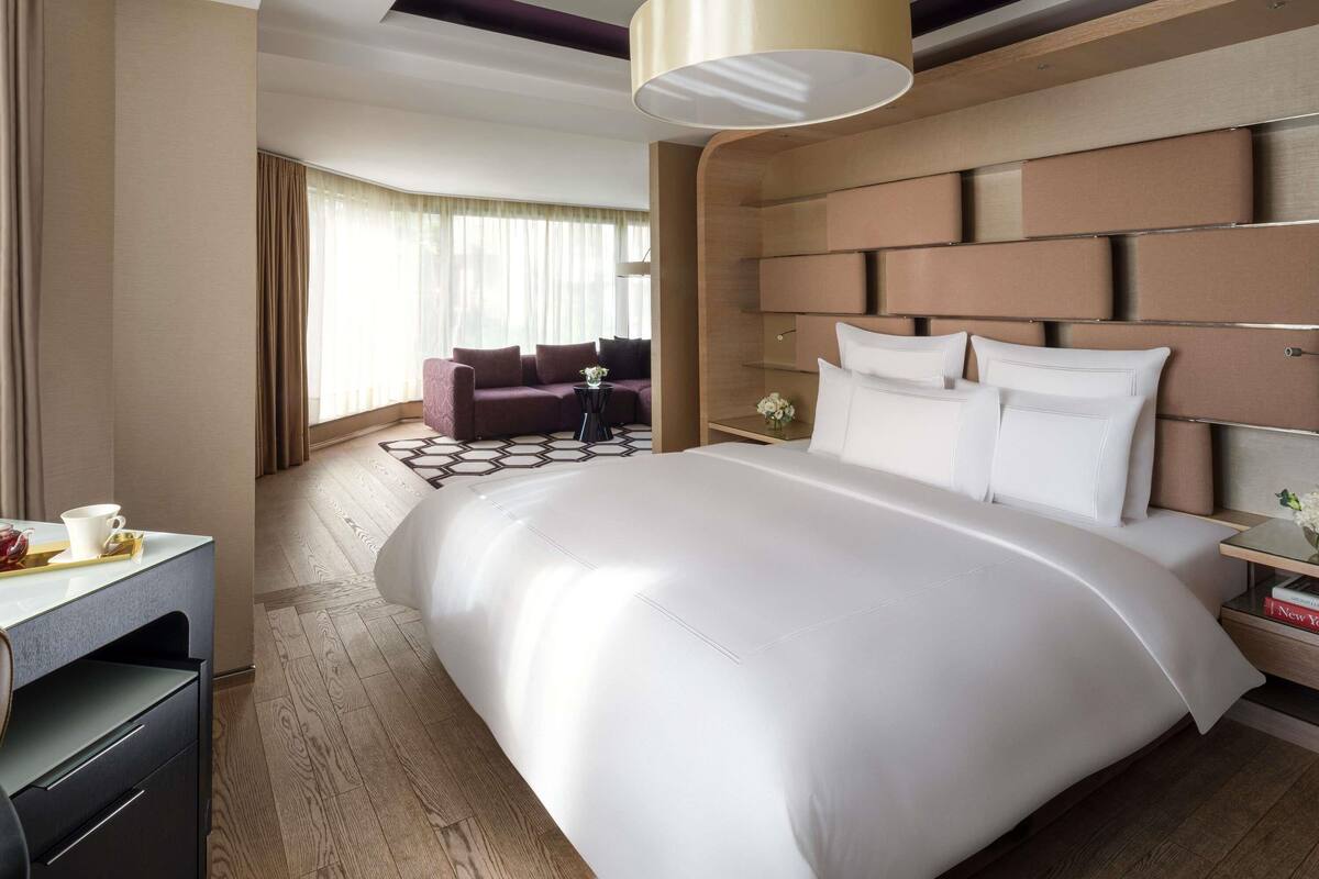 A hotel room with a large bed, a sofa, a desk with a chair, a lamp, and a view of the outdoors.
