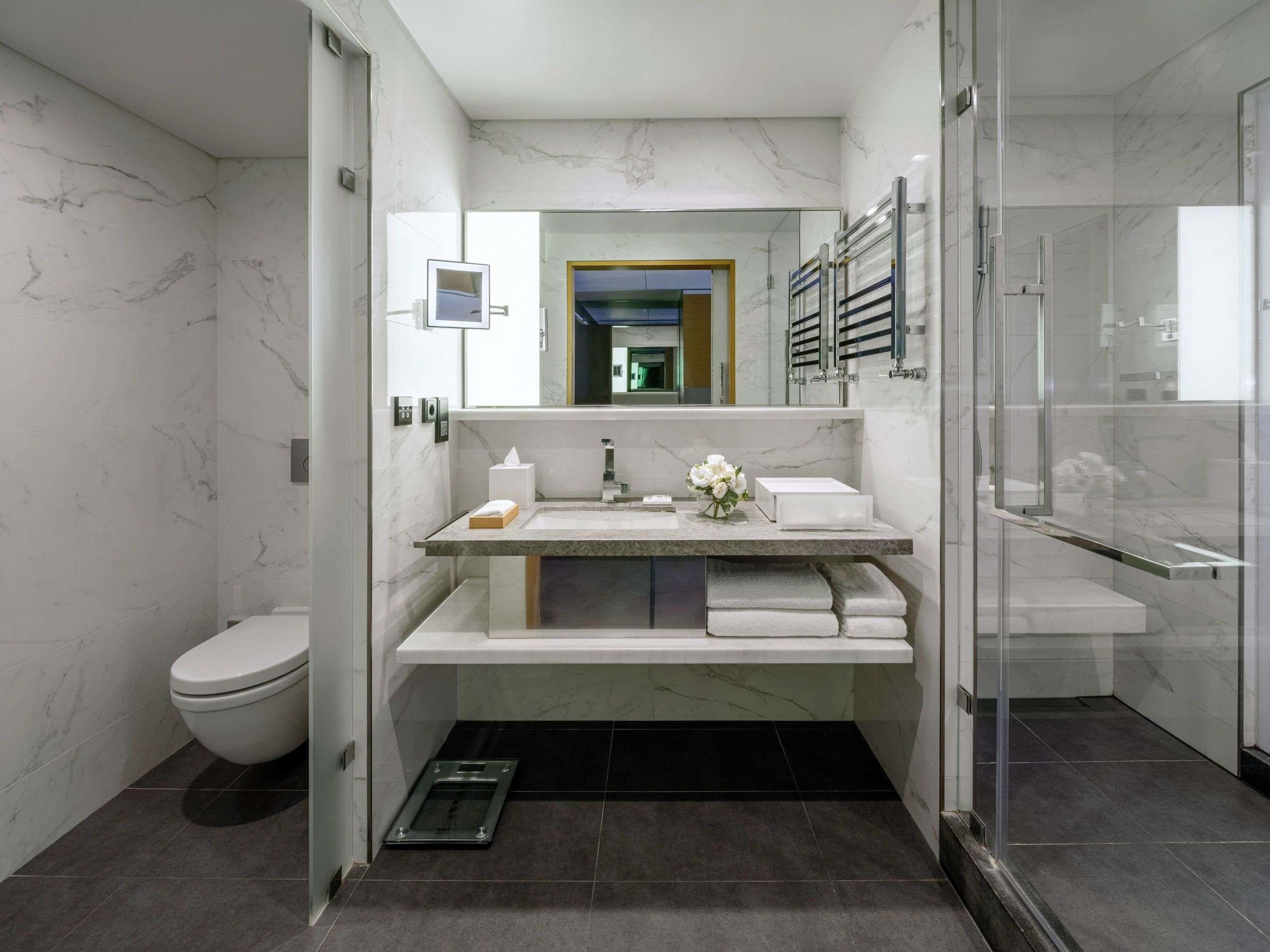A modern bathroom with a marble vanity, a toilet, a shower area, and a glass-enclosed shower stall.