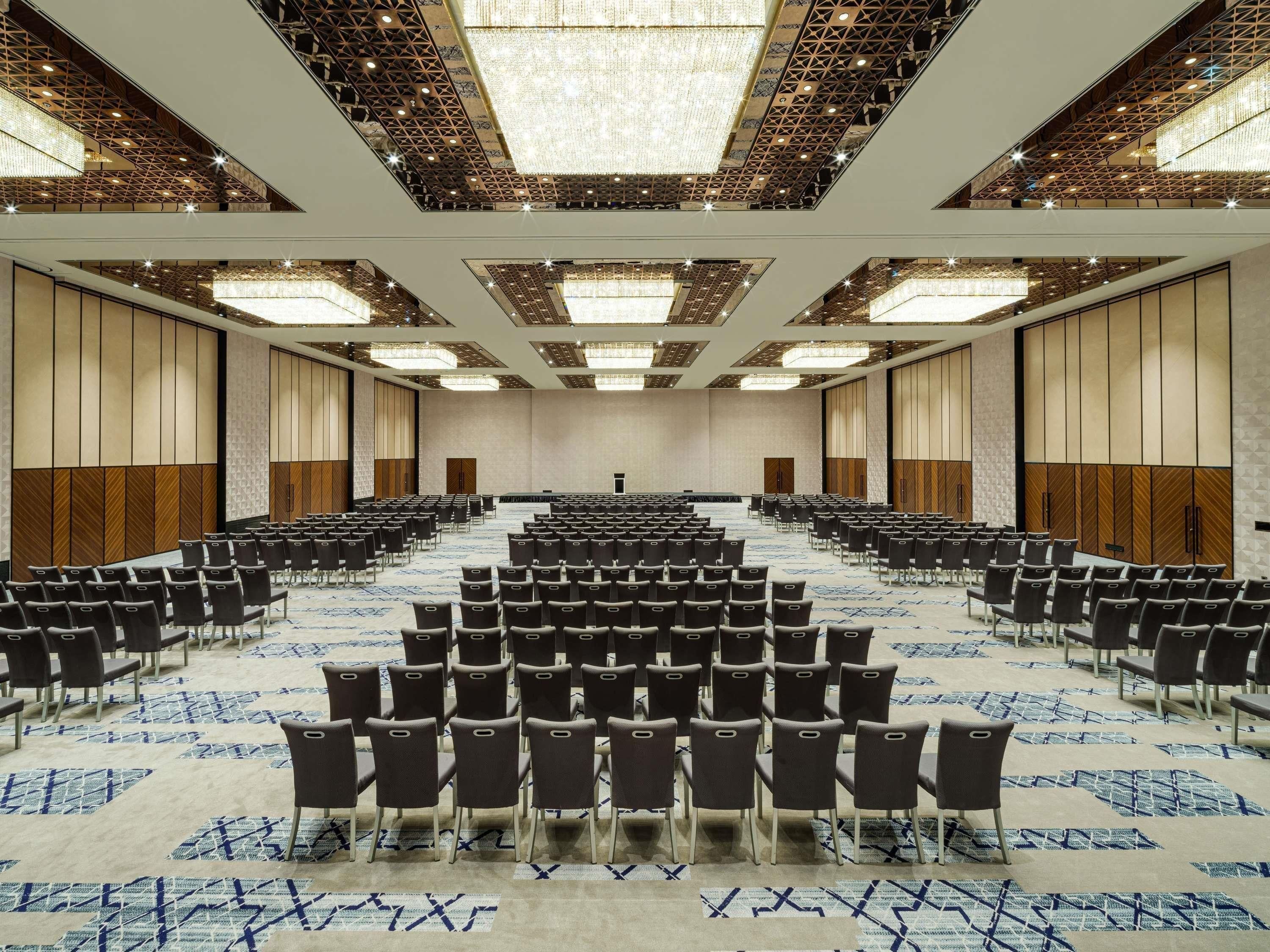 A large conference room with rows of chairs, a stage, and a patterned carpet.