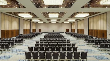 A large conference room with rows of chairs, a stage, and a patterned carpet.
