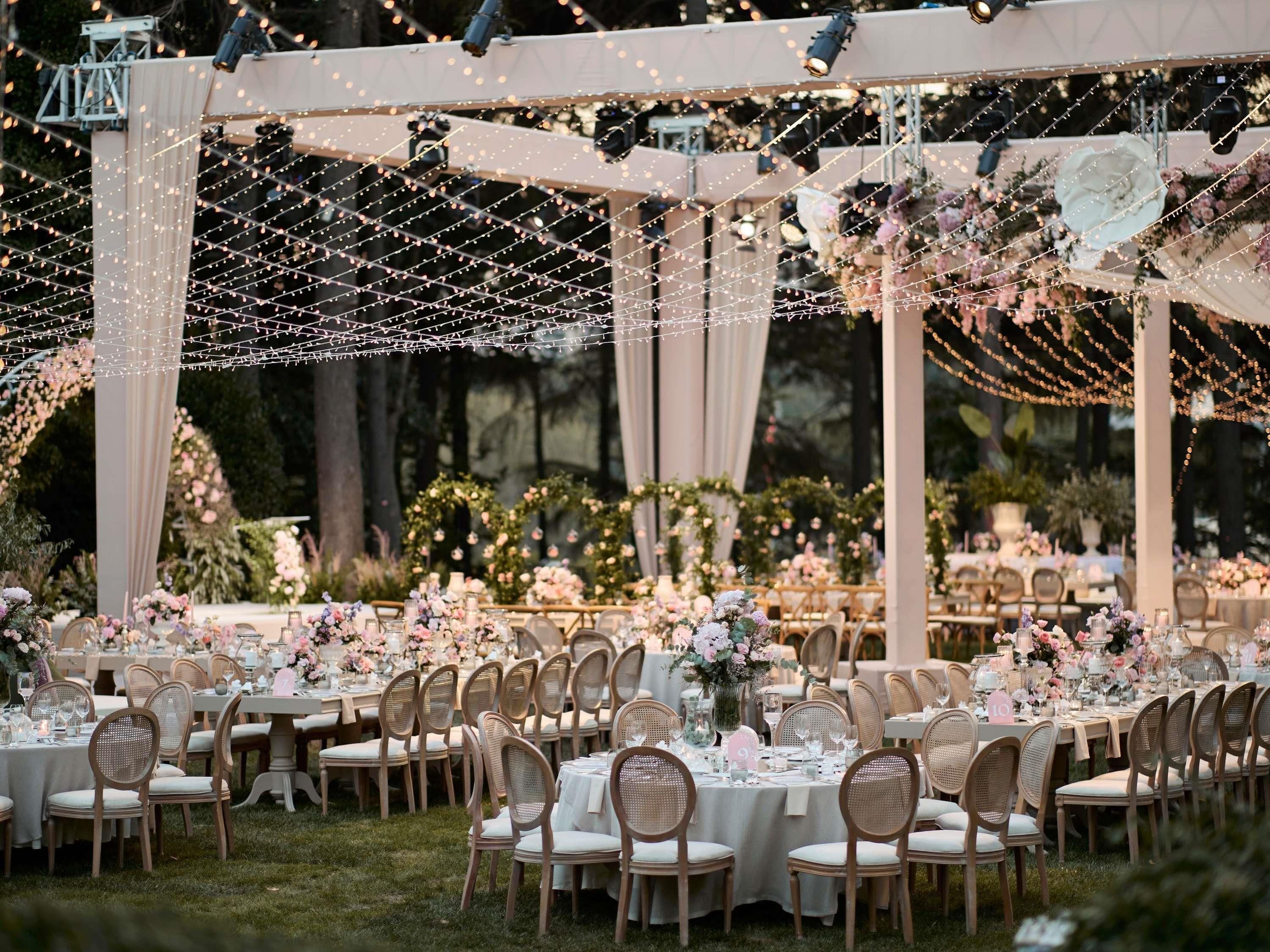 Een evenementenruimte buiten, met tafels gedekt voor gasten, omgeven door groen en bloemdecoraties.