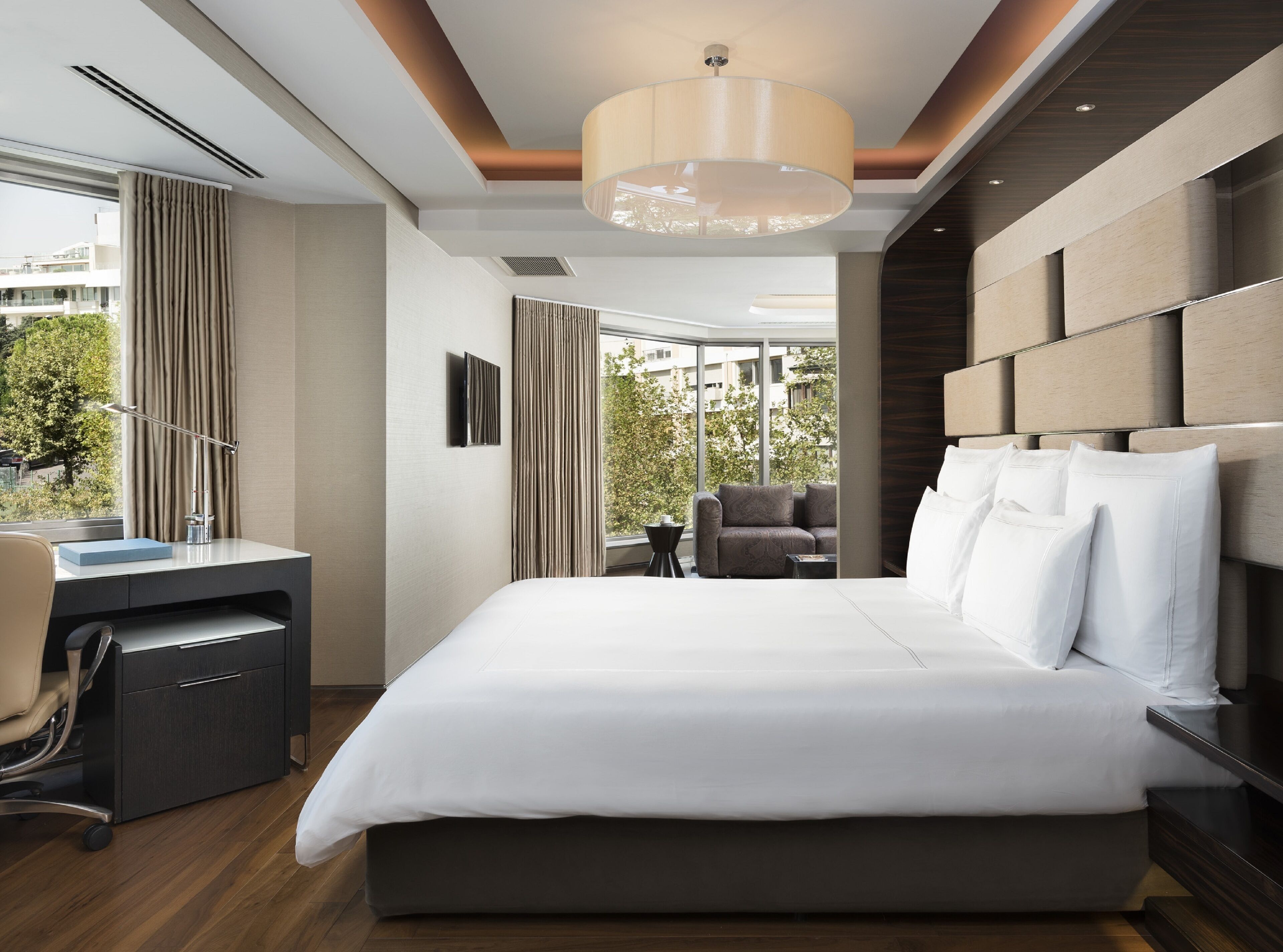 A modern hotel room with a large bed, a desk, and a view of the city.