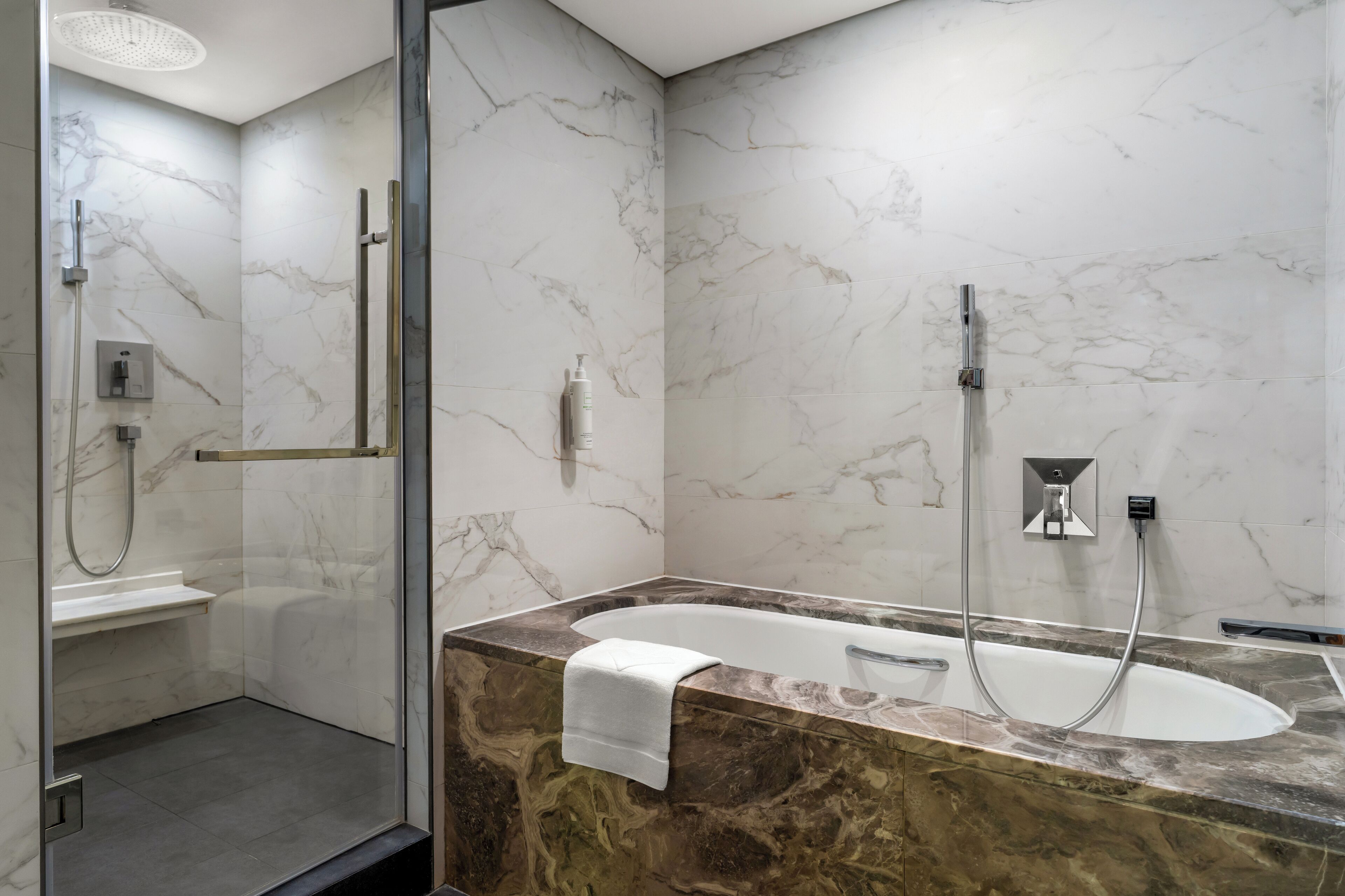 A modern bathroom with a glass-enclosed shower, a freestanding bathtub, and marble walls.