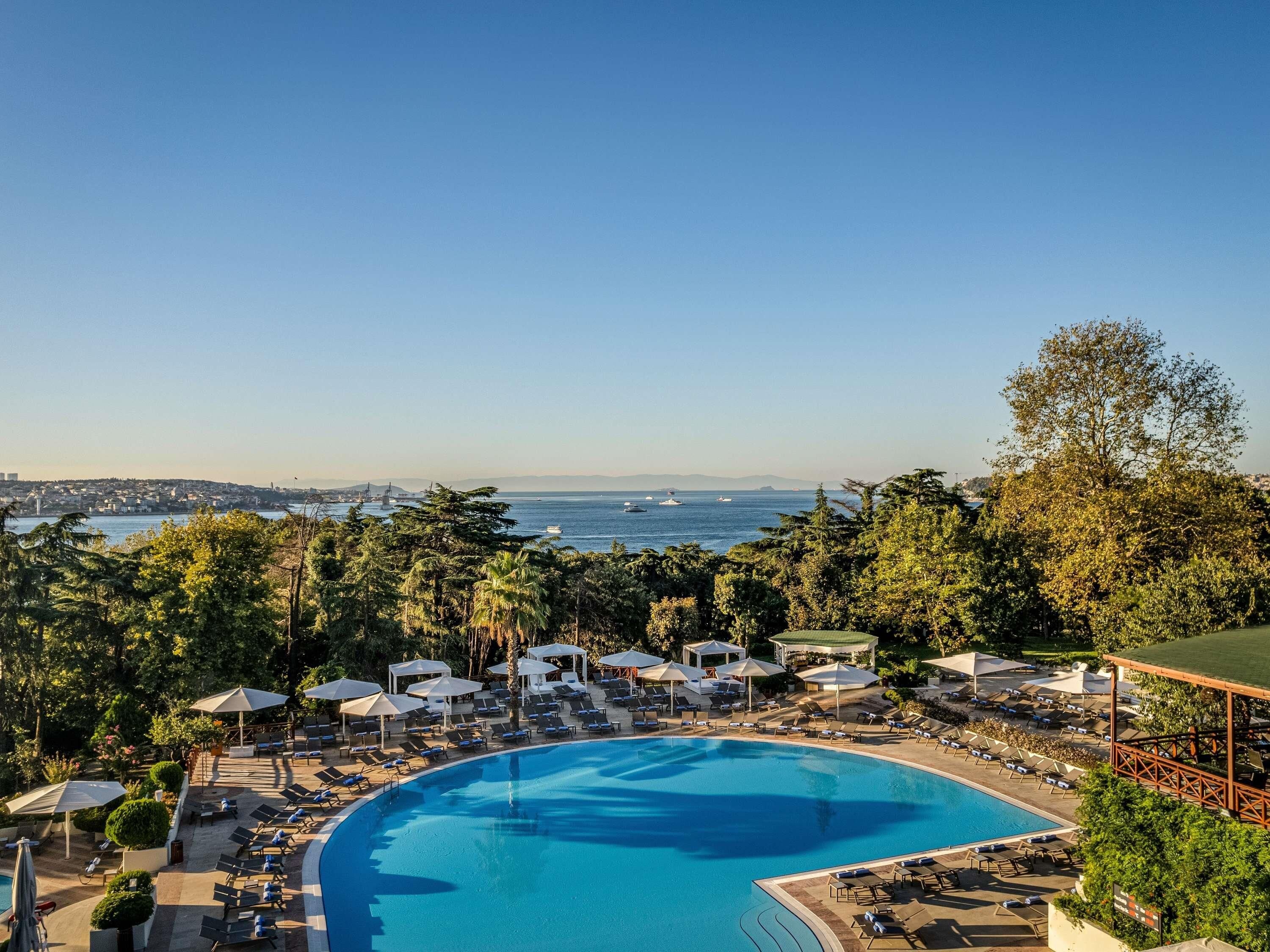 A resort with a large pool, lounge chairs, umbrellas, and a view of the sea.