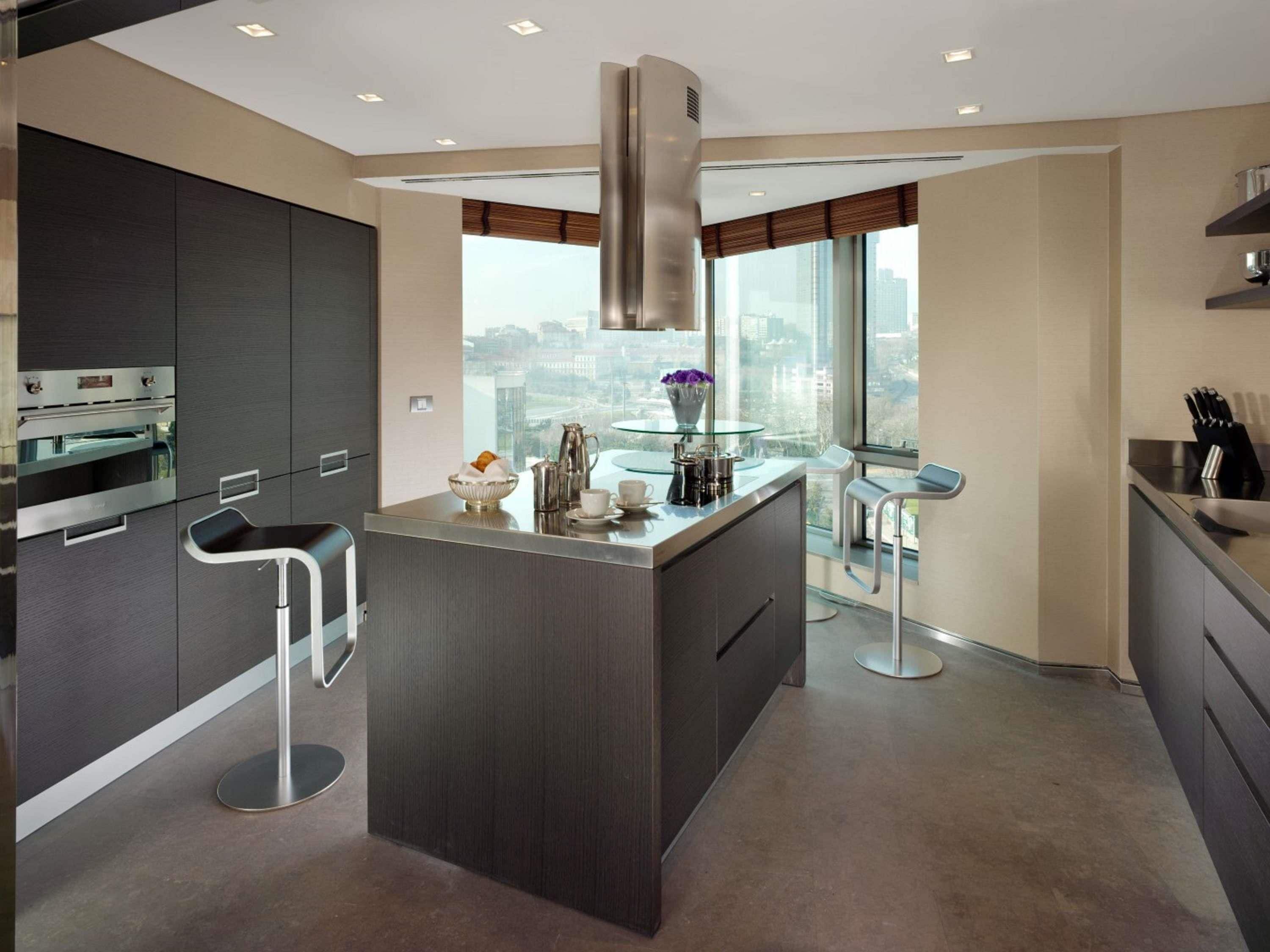 A modern kitchen with a central island, built-in oven, and a view of the city through large windows.