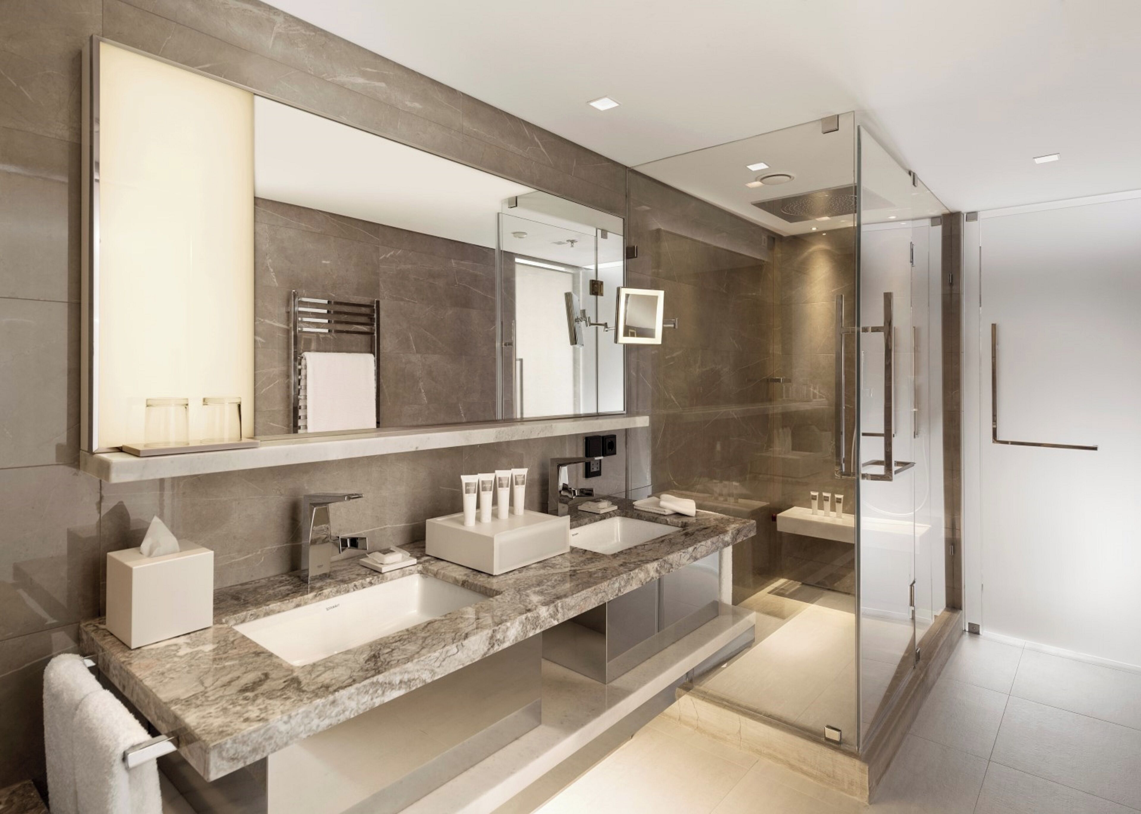 A modern bathroom with a large mirror, two sinks, and a glass-enclosed shower.