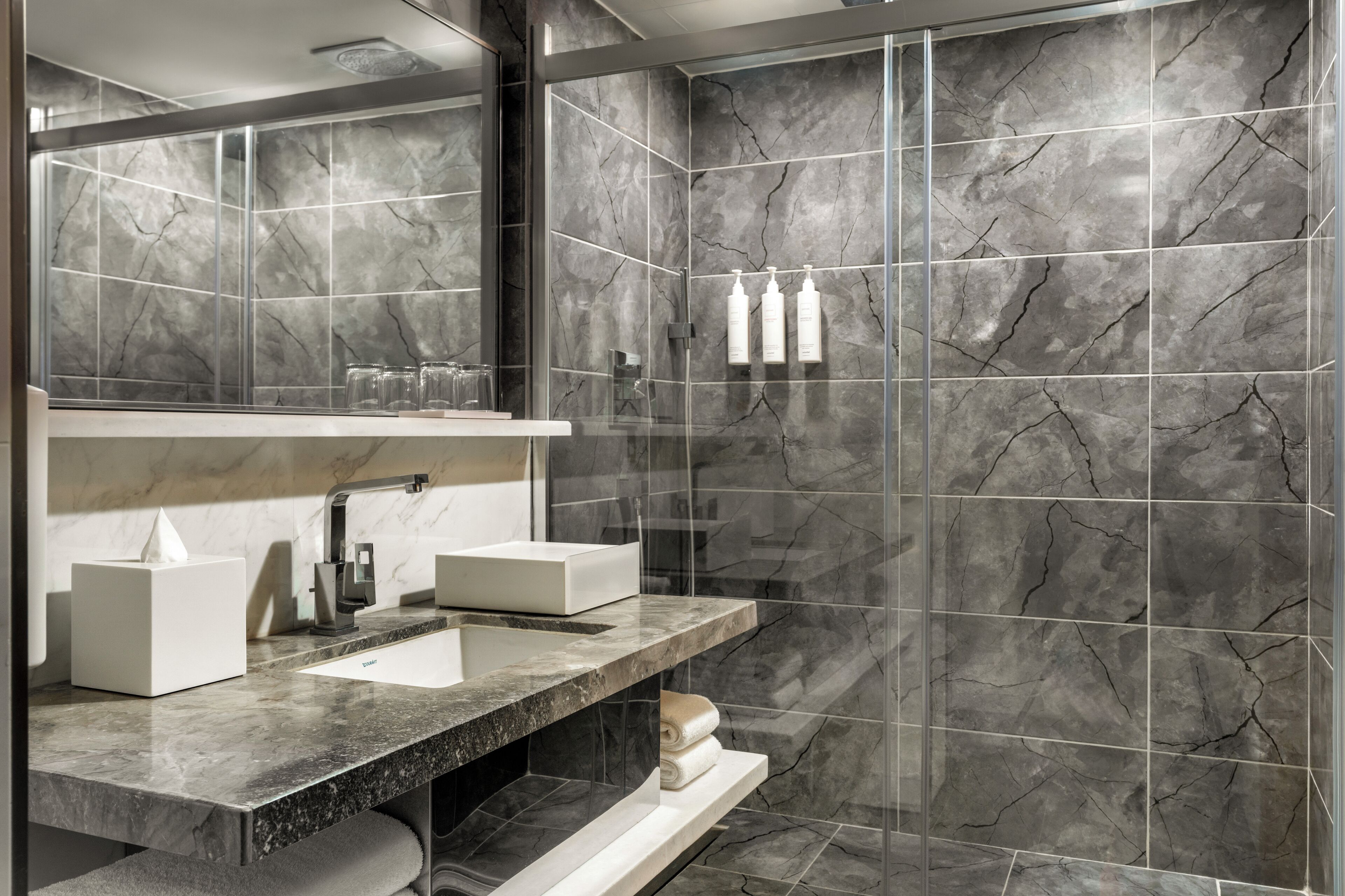 Un baño moderno con lavamanos de mármol, un espejo grande y una cabina de ducha de vidrio.