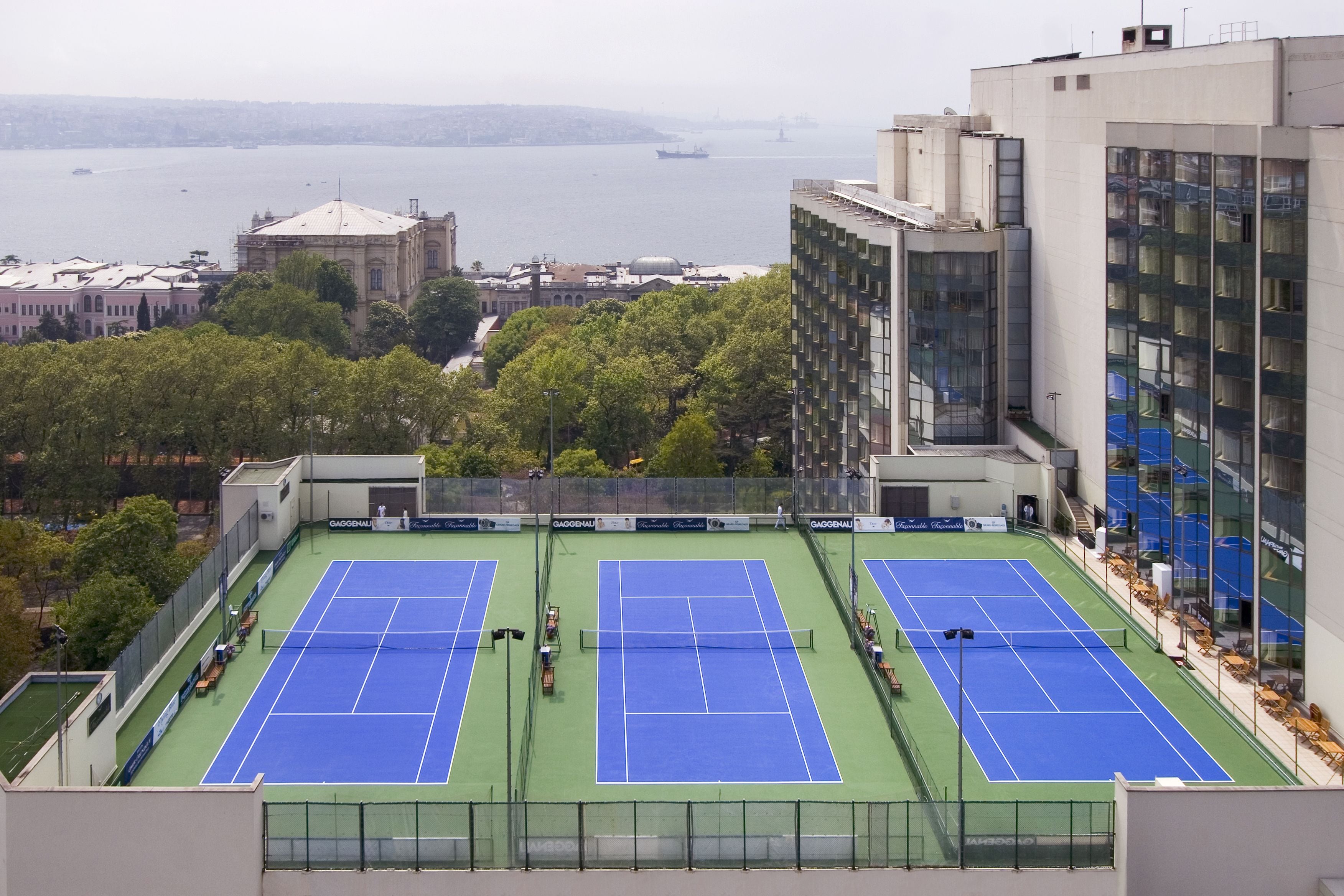 A tennis court with a cityscape view, surrounded by buildings and trees.