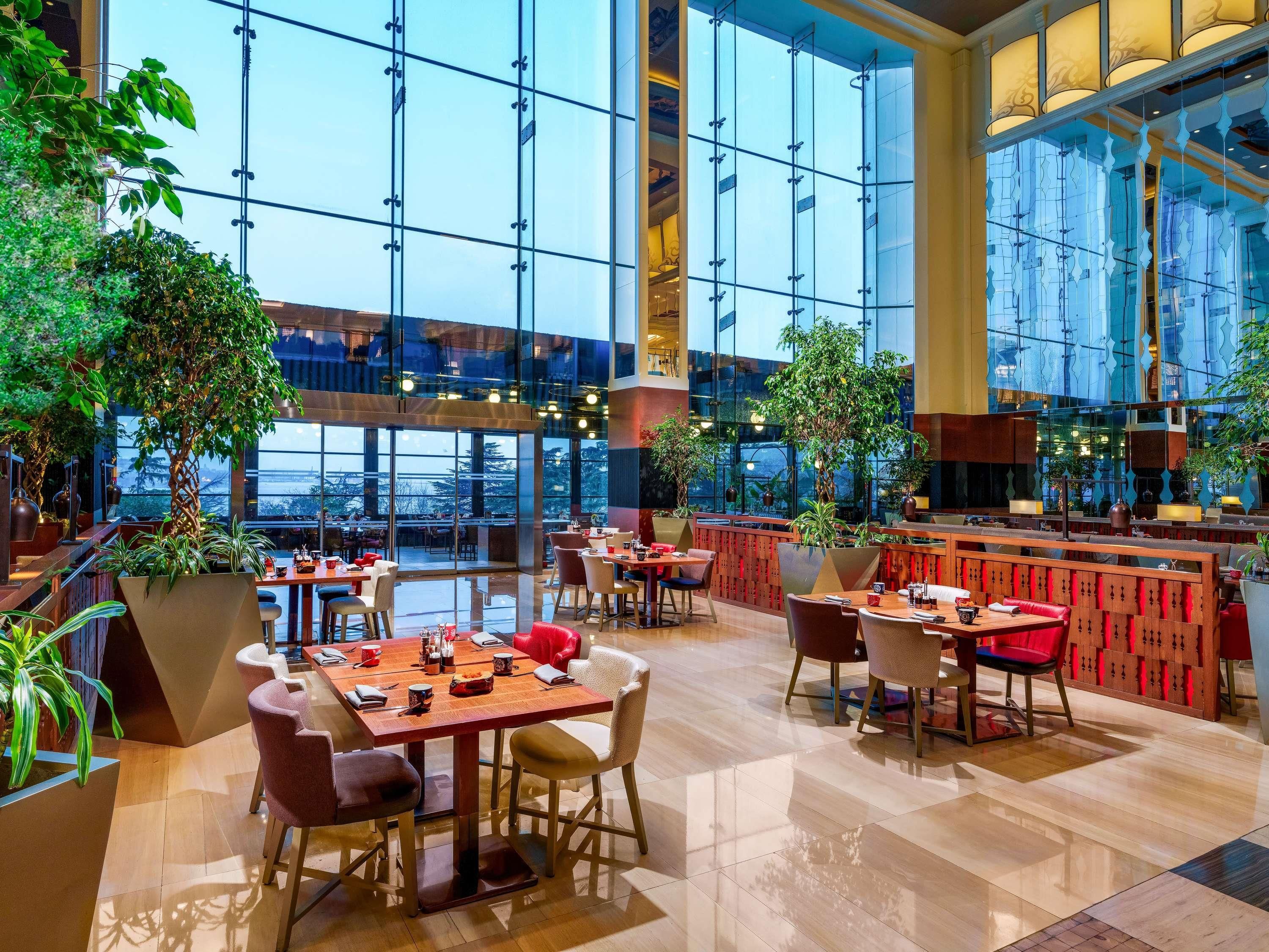 A spacious indoor dining area with high ceilings, large windows, and multiple seating arrangements.