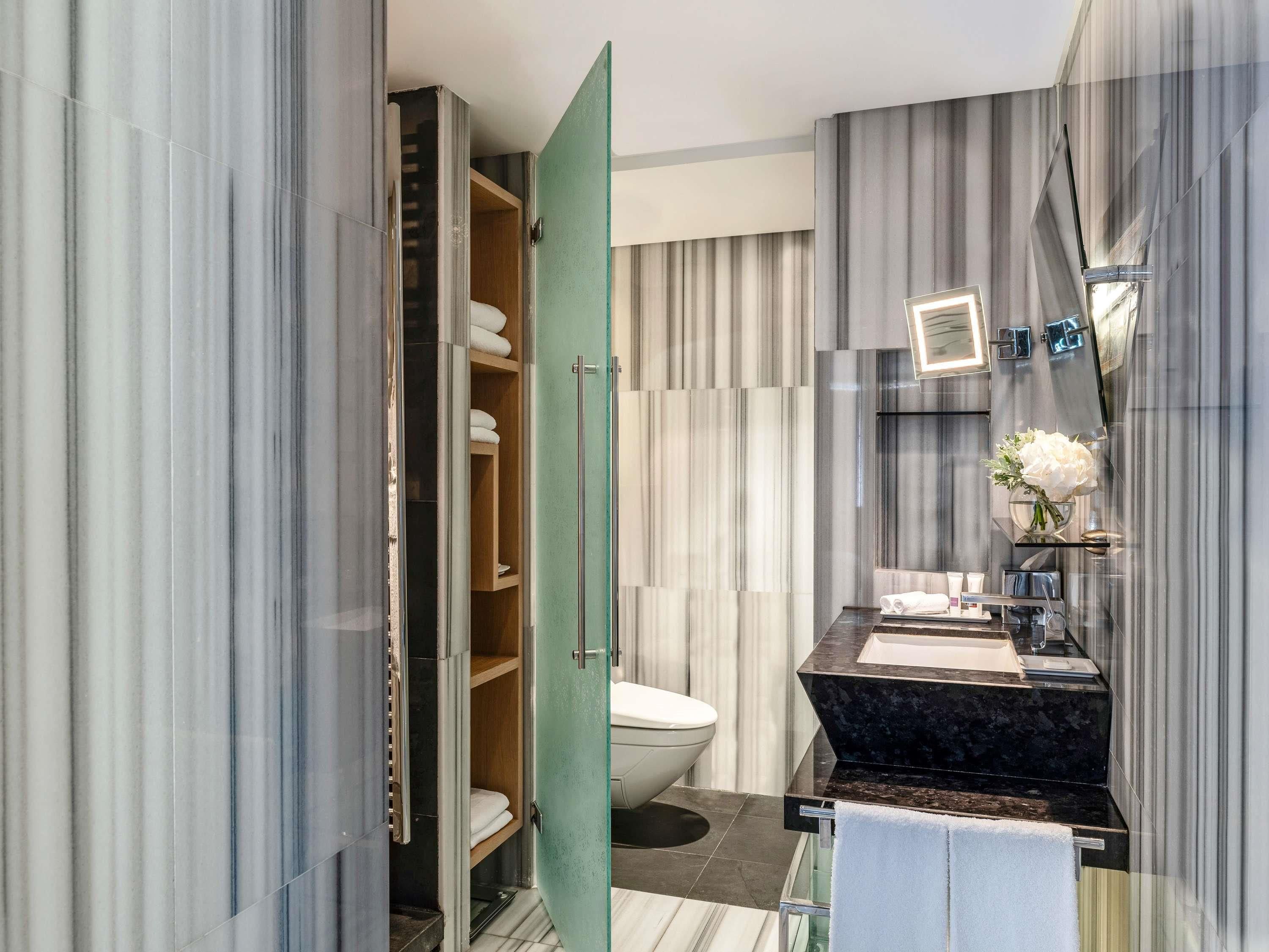 A modern bathroom with a marble vanity, a toilet, and a walk-in closet.