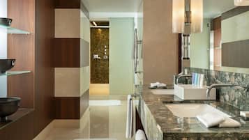 A modern bathroom with a large mirror, two sinks, a glass shelf, and a shower area.