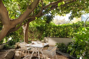 An outdoor patio with a table and chairs, surrounded by greenery and a tree.