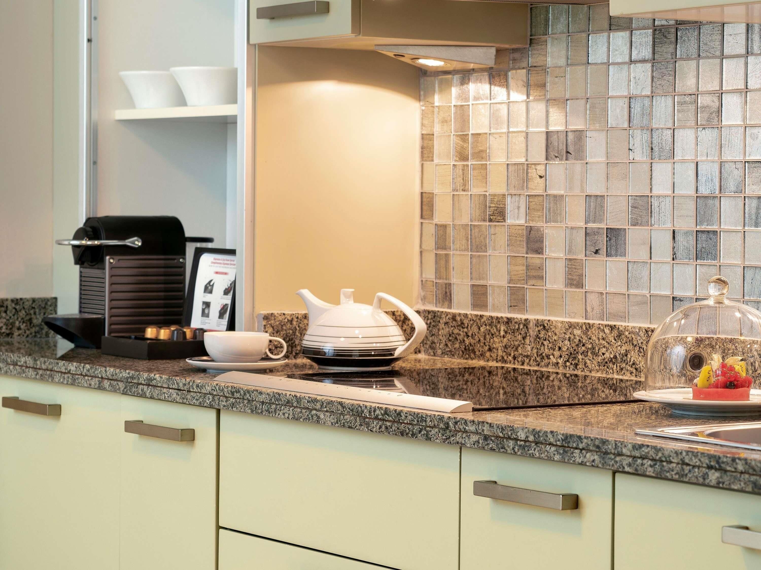 A kitchen with a coffee machine, teapot, and a fruit display on the counter.