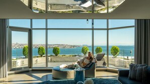 A spacious living room with large windows, a modern ceiling fan, and a view of the sea and cityscape. - Swissotel The Bosphorus Istanbul (Istanbul)