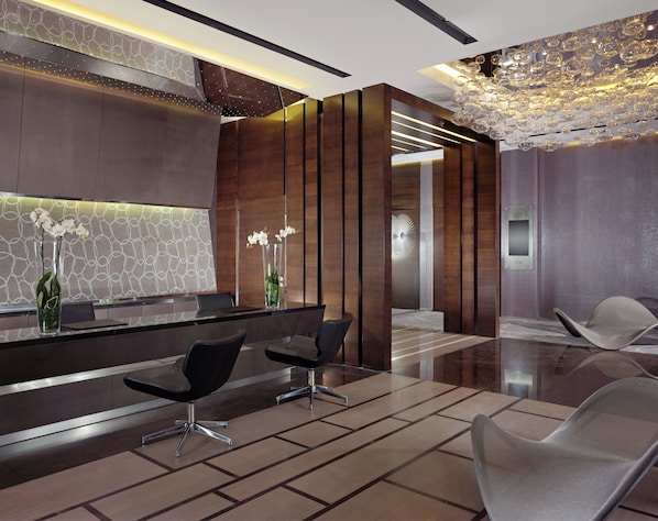 A modern reception area with a marble reception desk, two black chairs, a vase with white flowers, and a decorative ceiling light. - Swissotel The Bosphorus Istanbul (Istanbul)