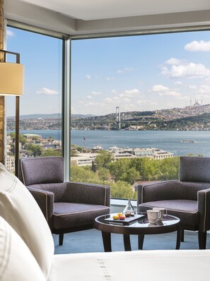 A modern room with a large window offering a view of a bridge and cityscape. There are two upholstered chairs and a small round table with a teapot and pastries. - Swissotel The Bosphorus Istanbul (Istanbul)