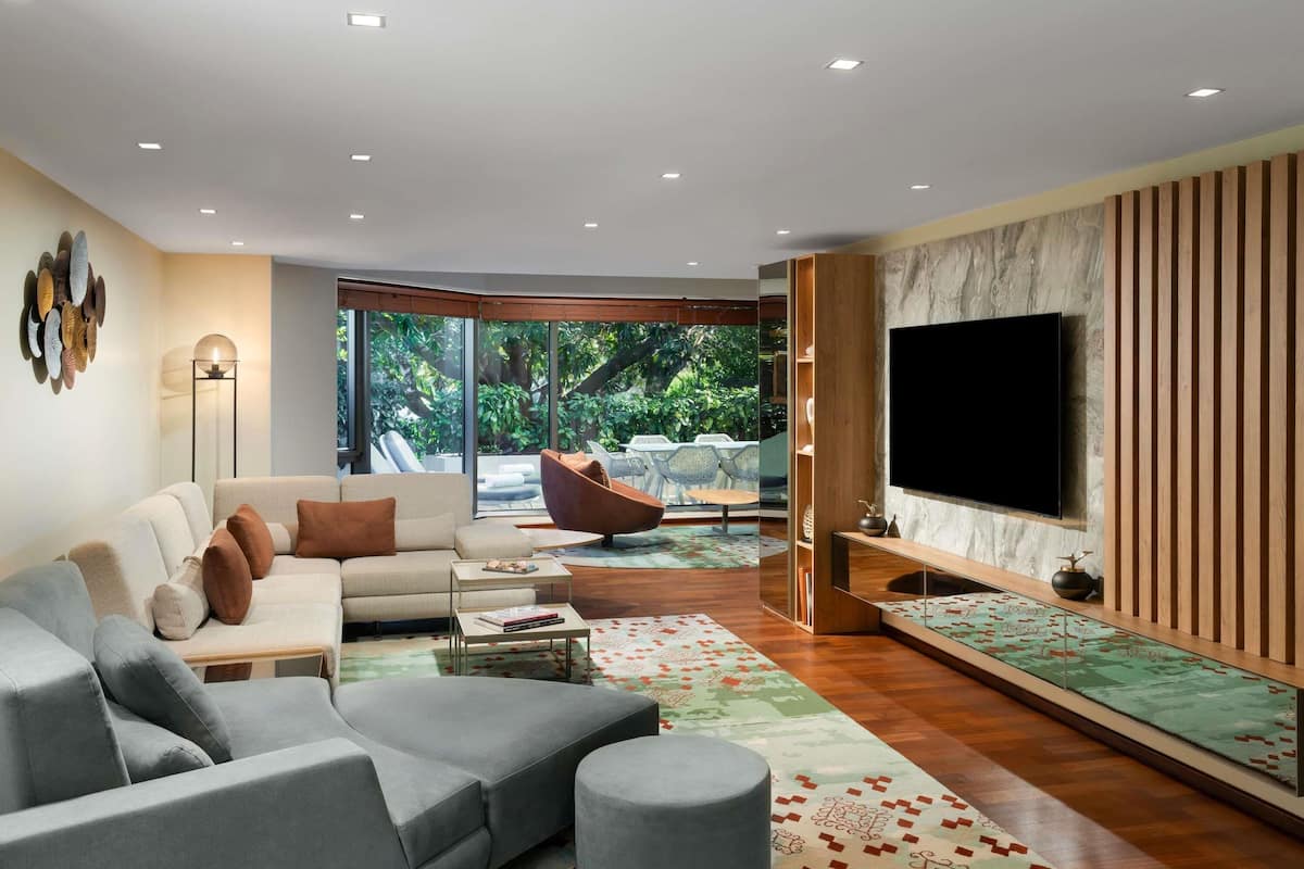 A modern living room with a sofa, coffee table, TV, and a large window overlooking greenery.