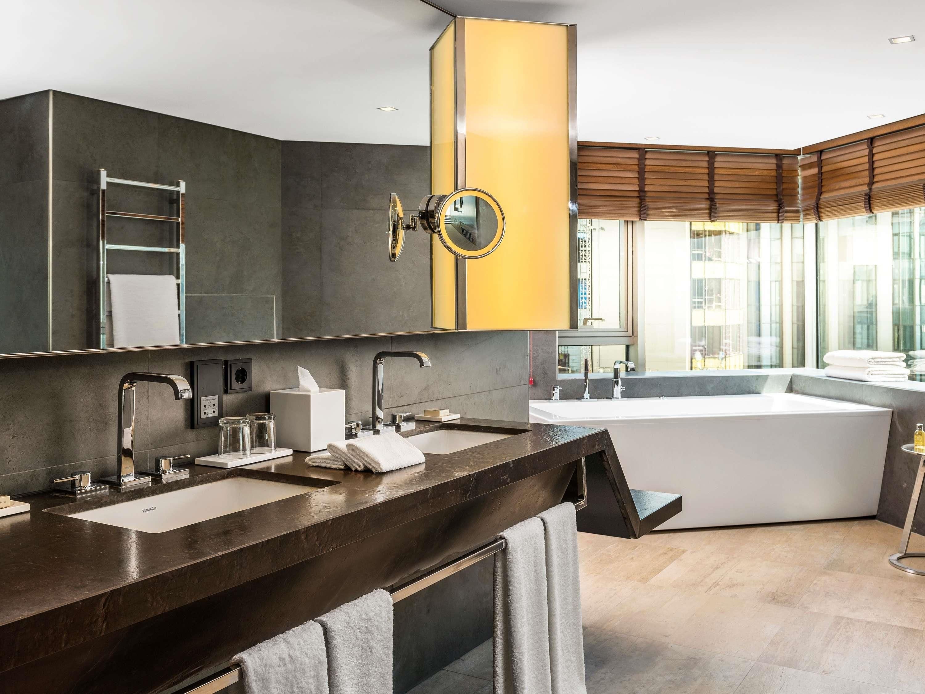 A modern bathroom with a large mirror, a bathtub, and a vanity with two sinks.