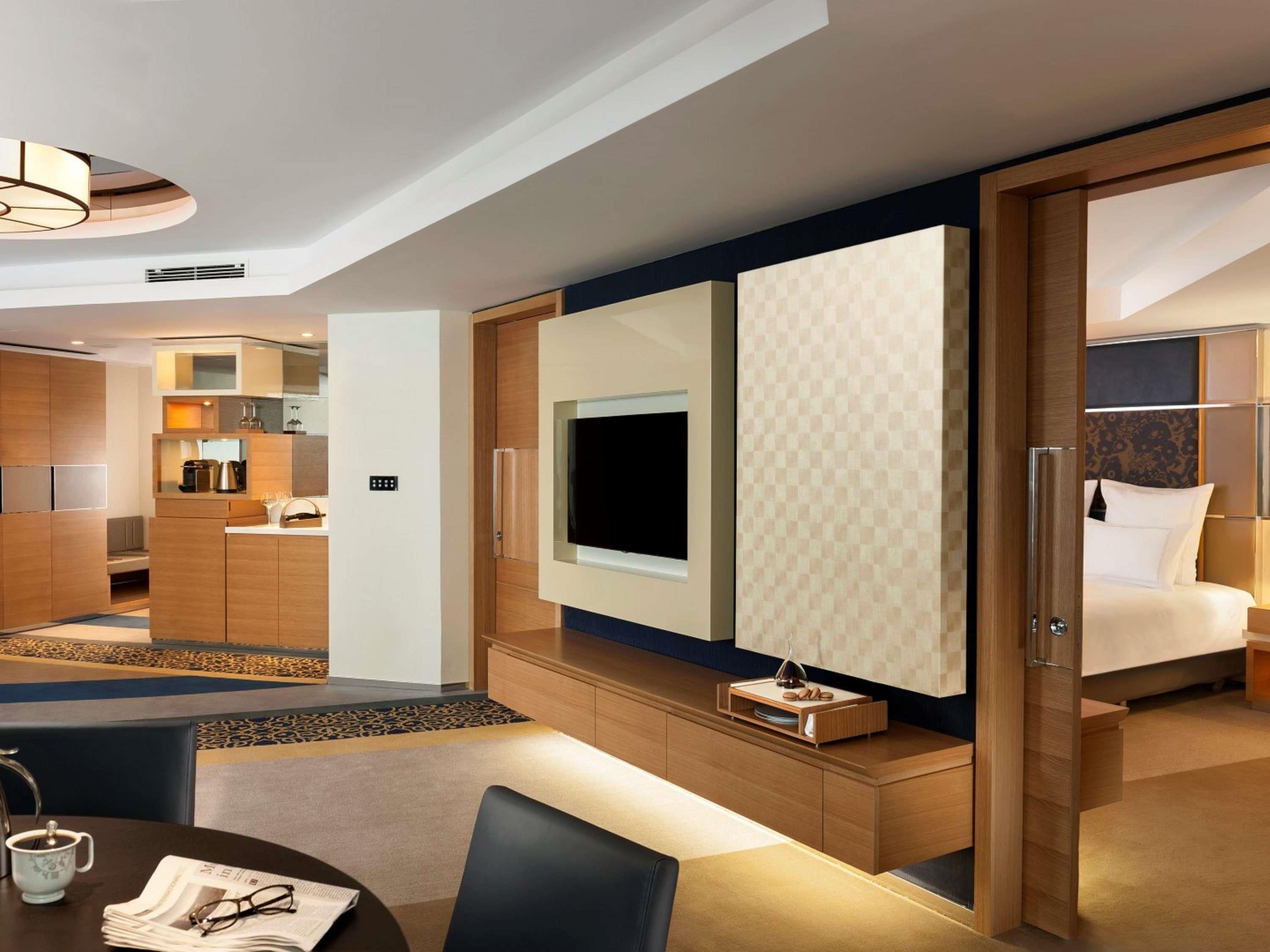 A modern hotel room with a dining area, kitchenette, and a large bed.