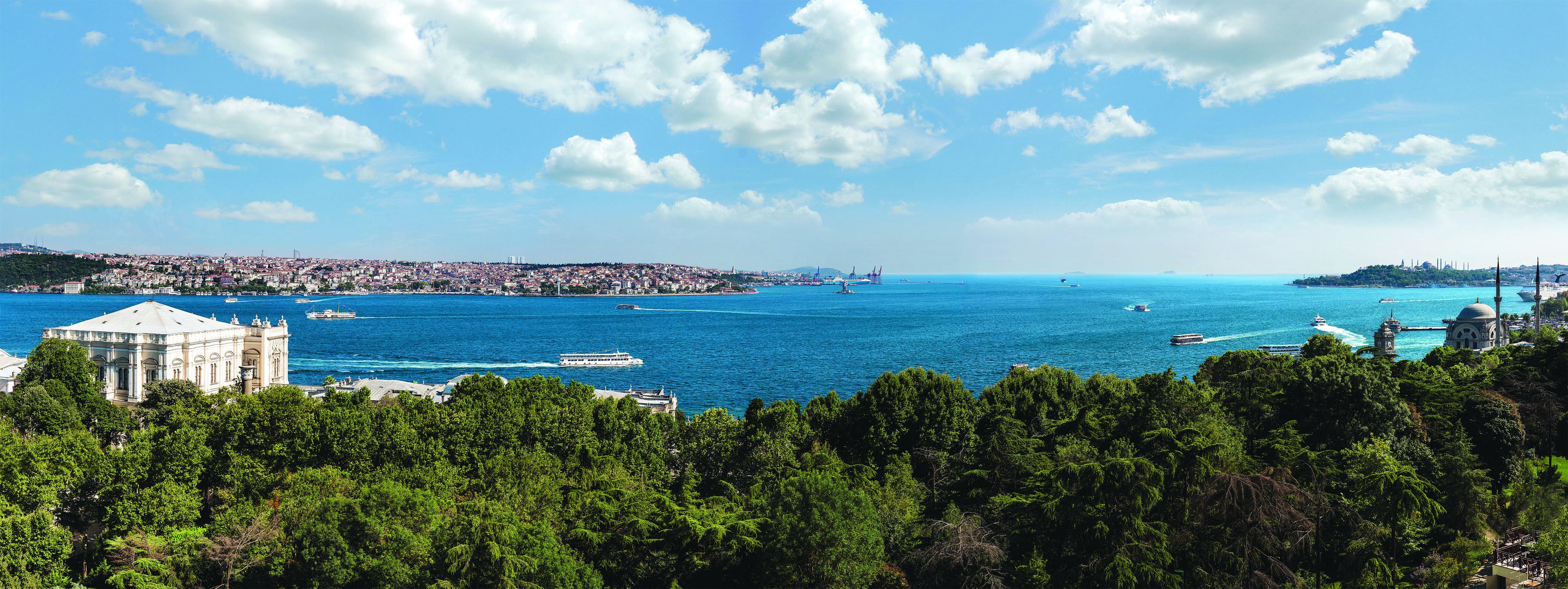 Eine Küstenstadt mit einem markanten historischen Gebäude, blauem Himmel und Blick auf das Meer mit Booten.