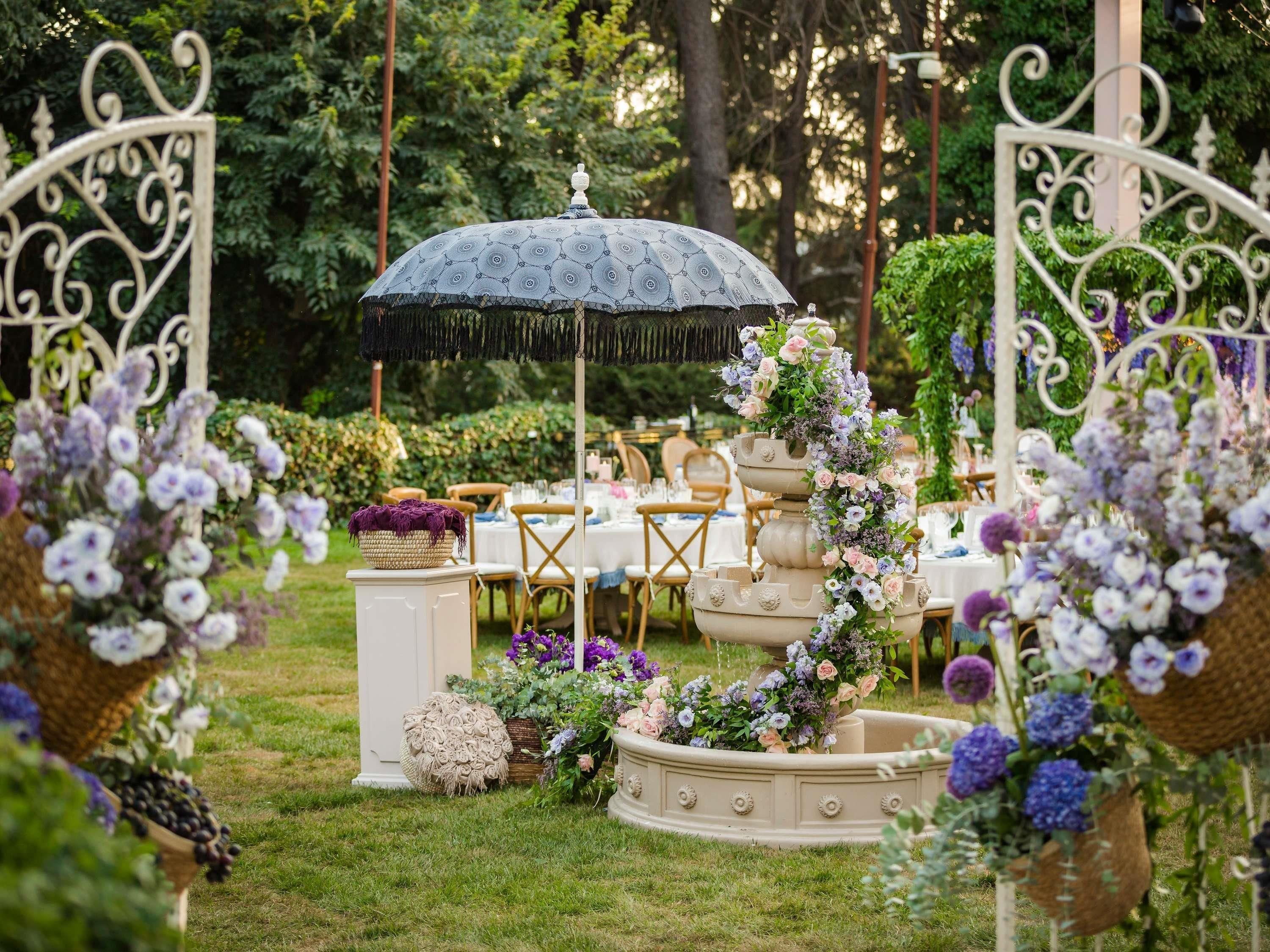 Un espace extérieur aménagé en jardin, avec une fontaine décorative, des tables et des chaises disposées pour un événement.