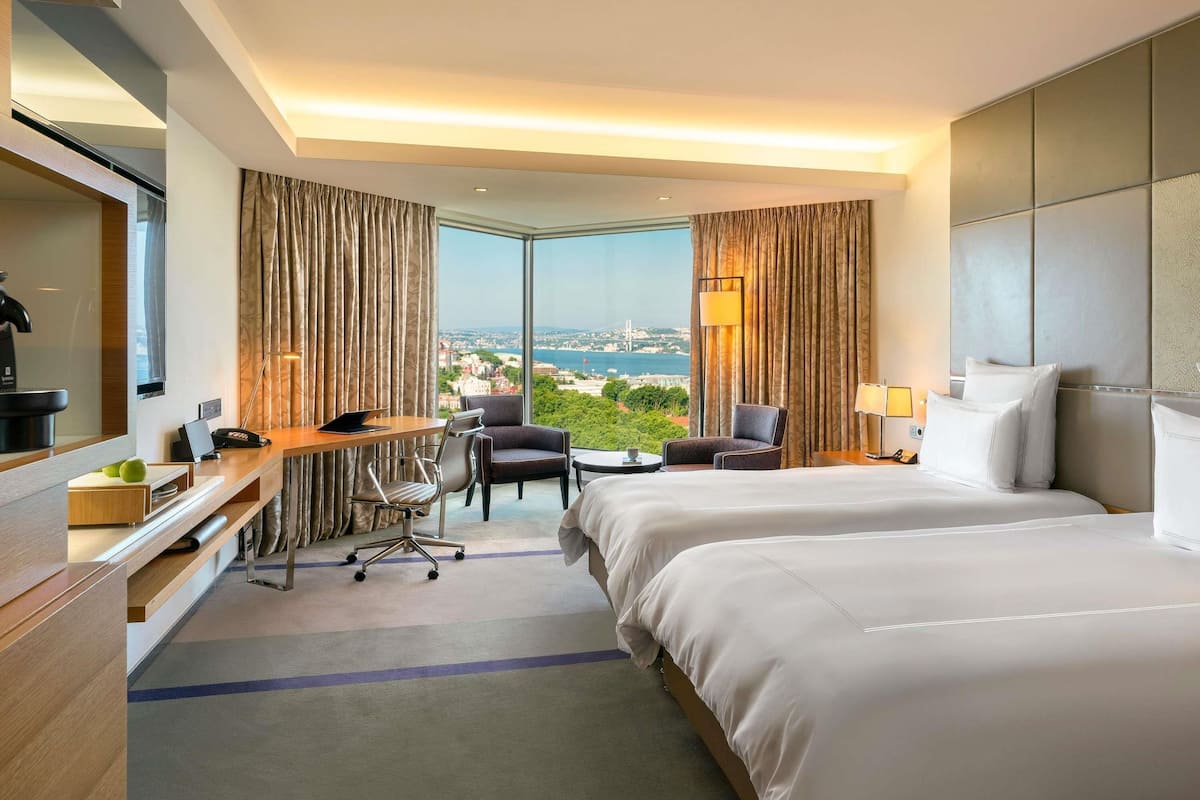 A hotel room with a large bed, a desk, a chair, and a view of a cityscape.