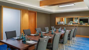 A conference room with a long table, chairs, a wooden door, a mirror, and a kitchenette area.