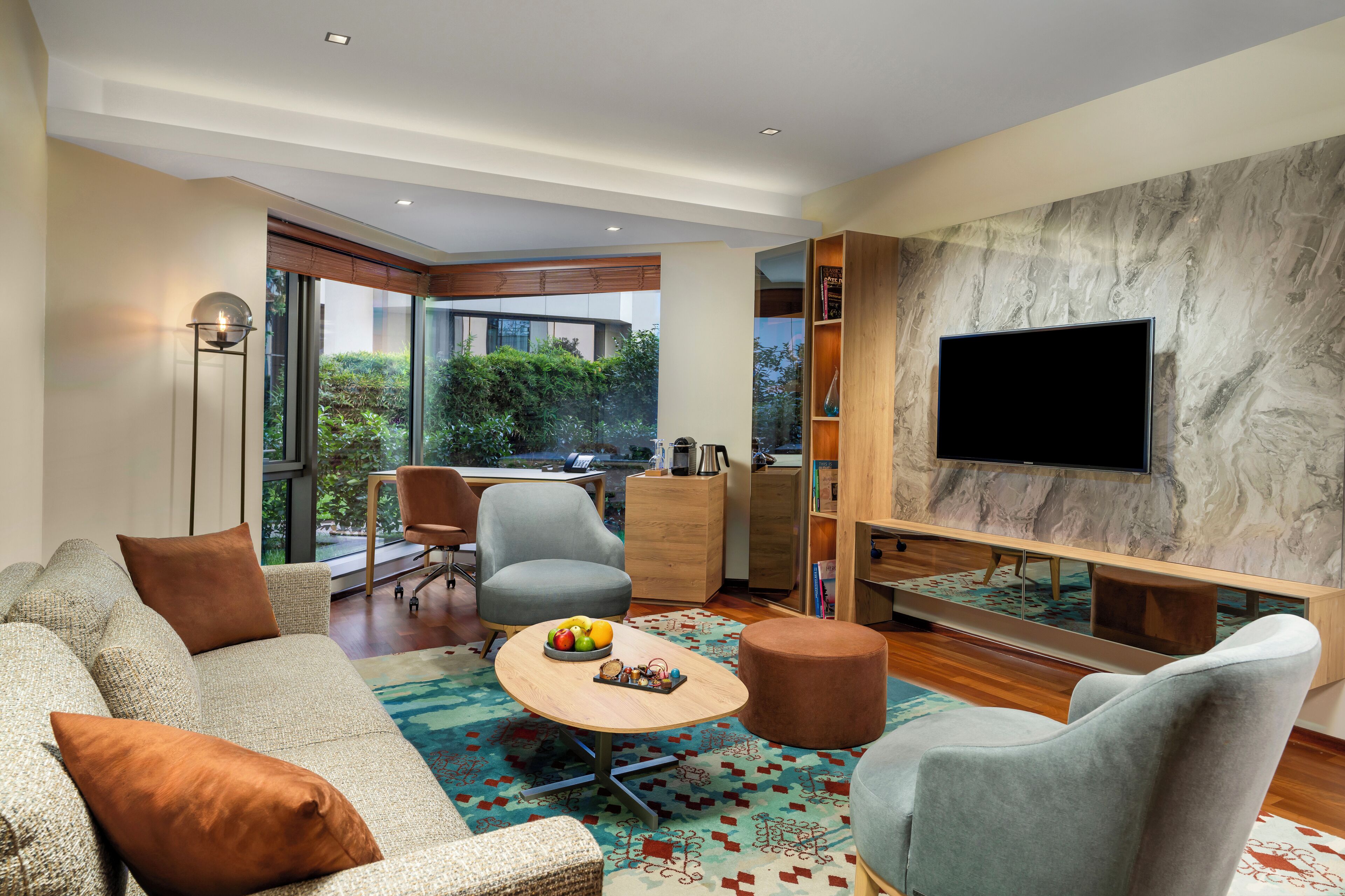 A modern living room with a sofa, armchairs, a coffee table, and a flat-screen TV mounted on a marble wall.