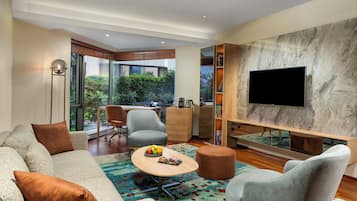 A modern living room with a sofa, armchairs, a coffee table, and a flat-screen TV mounted on a marble wall.