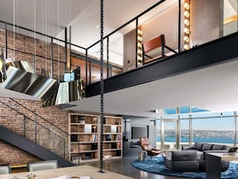 Ein modernes Interieur mit Treppe, einer großen Bücherwand, einem Ledersessel und Blick auf die Stadt.