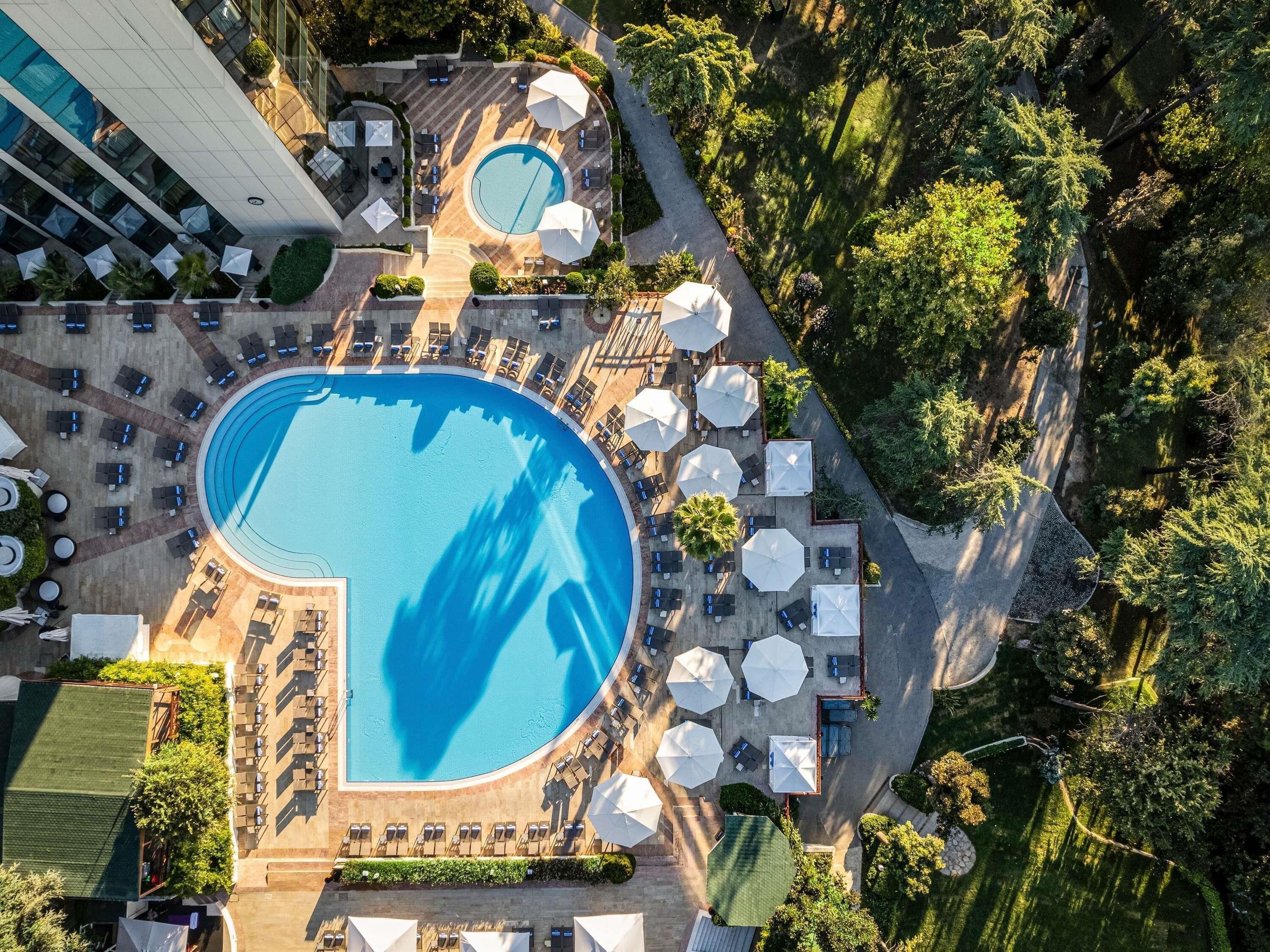 An aerial view of a hotel with a large swimming pool, sun loungers, and umbrellas.