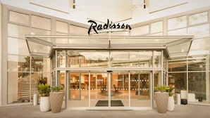 A modern Radisson hotel entrance with a glass facade, large potted plants, and a staircase leading to the upper floor. - Radisson Hotel Nice Airport (Nice)
